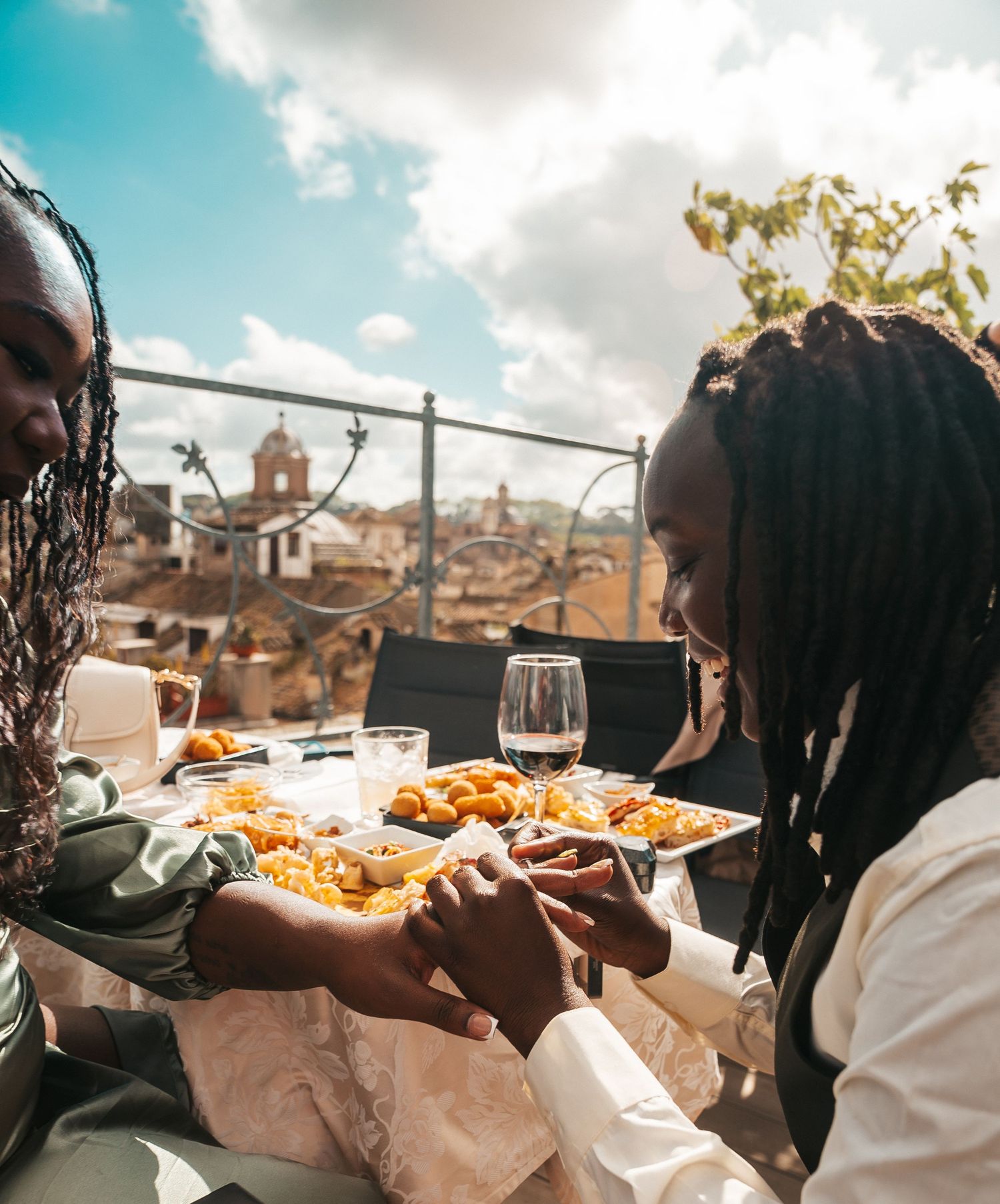 Rooftop dining scene with wine glasses and appetizers against Rome cityscape view.