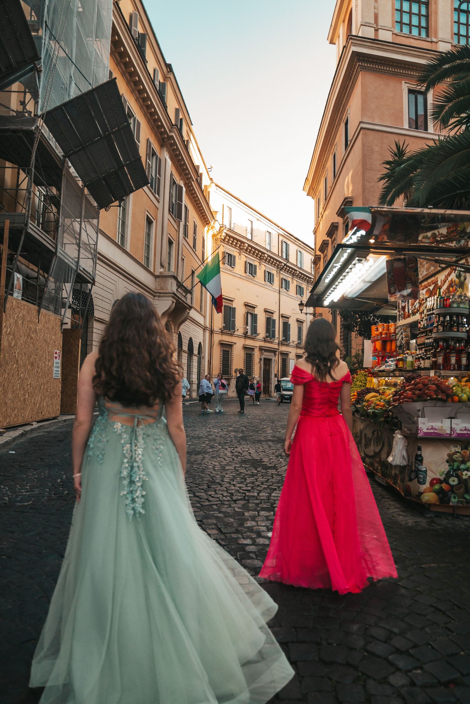 Two elegant dresses, one mint green and one red, flowing on the cobblestone streets of Rome.