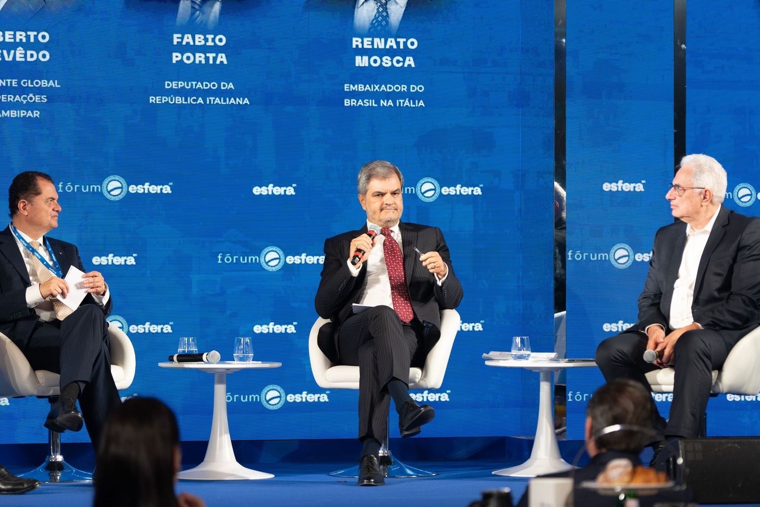 Panelists seated at a long table with blue backdrop during a conference or forum discussion.