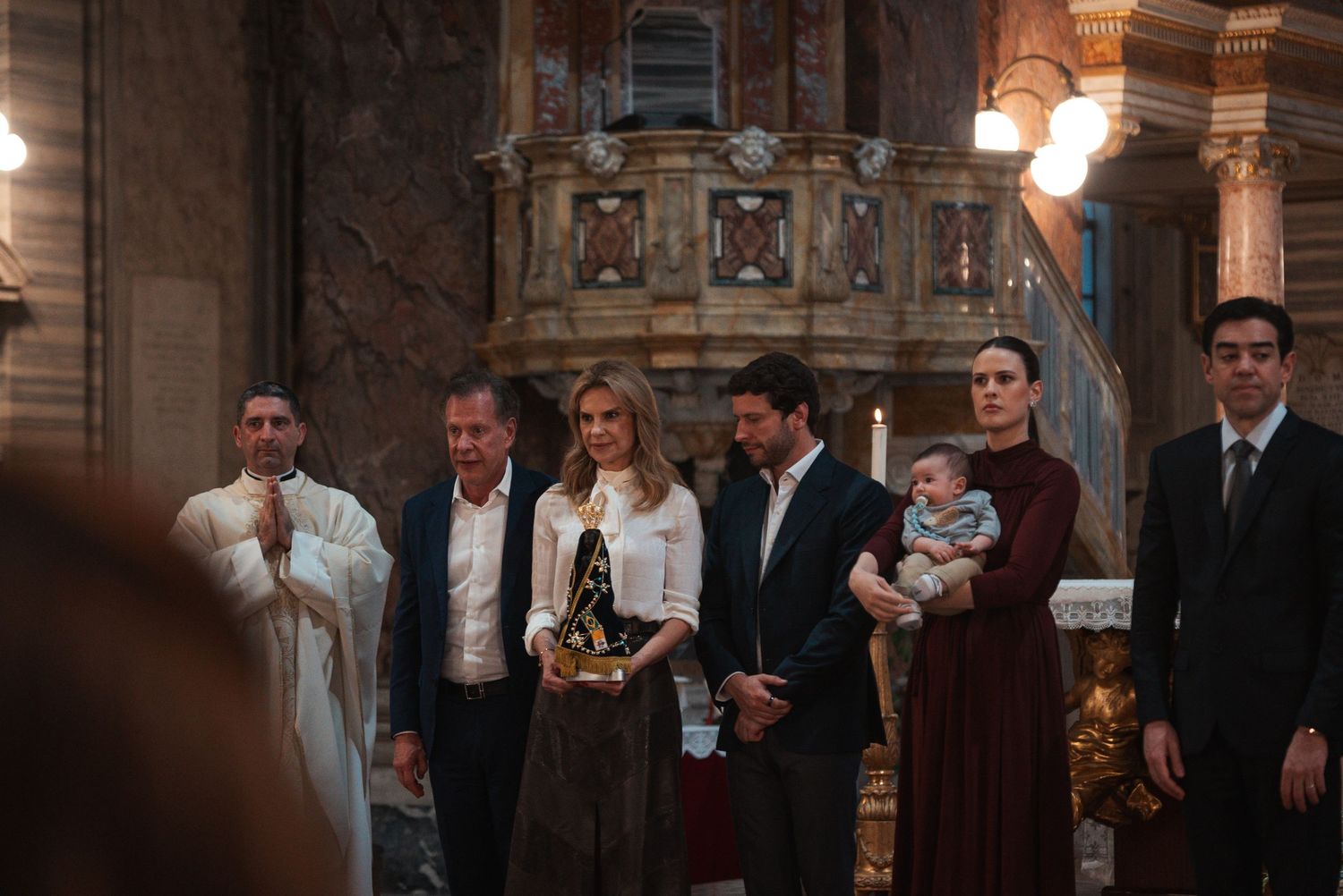 People in formal attire stand together in an ornate architectural space during a special event.