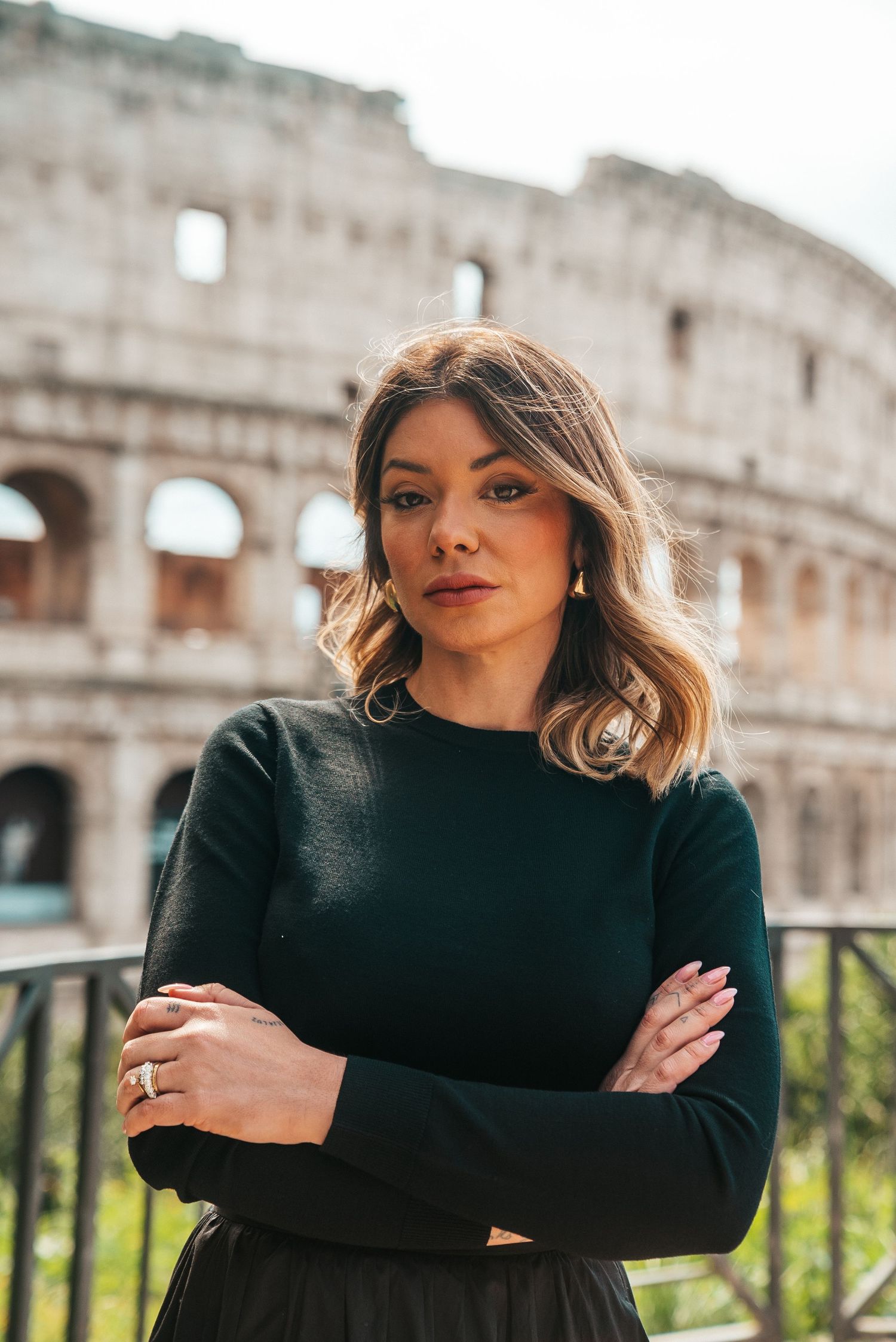 Black-clad figure poses in front of the ancient Colosseum in Rome.