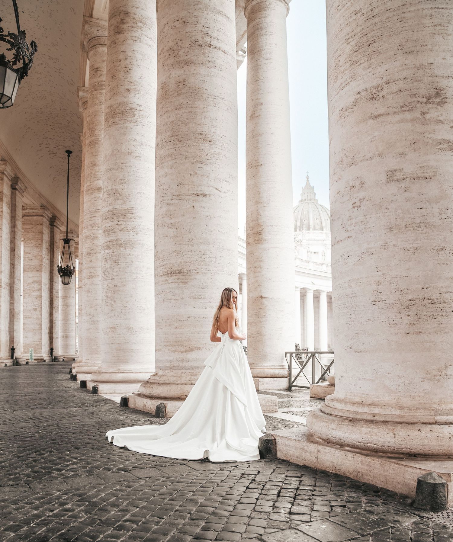 Bride in flowing white gown poses among the majestic columns of Vatican City.