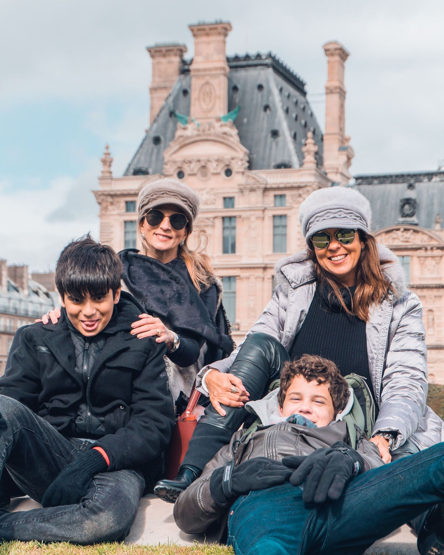 A group relaxes together on the grass outside the Louvre Museum in Paris on a sunny day.