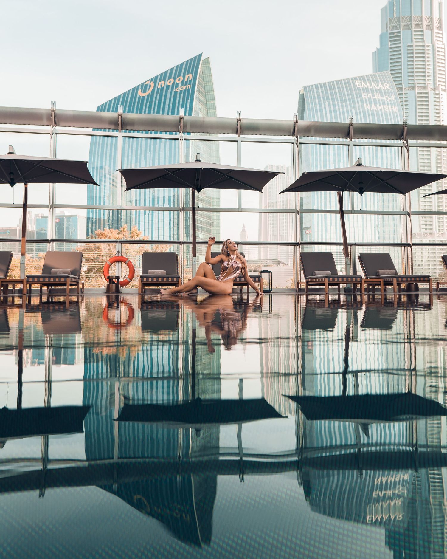 Panoramic view of a luxury rooftop infinity pool with lounge chairs overlooking a modern city skyline at sunset.