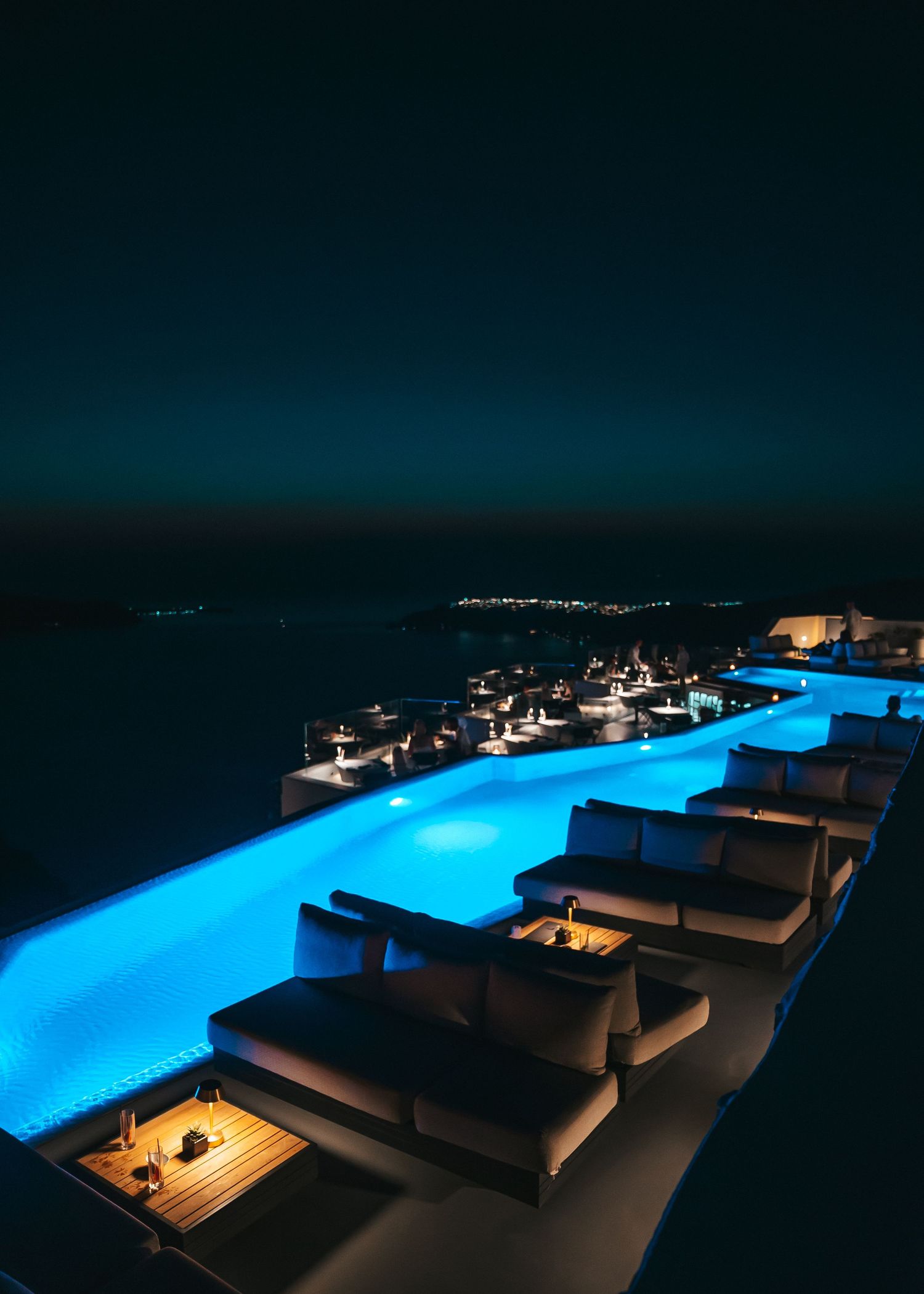 Luxurious infinity pool with illuminated blue water and lounge chairs overlooking a nighttime coastal view.