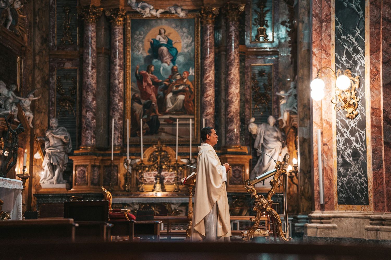 Ornate interior of a historic church with gilded baroque decorations and dramatic lighting illuminating the altar area.