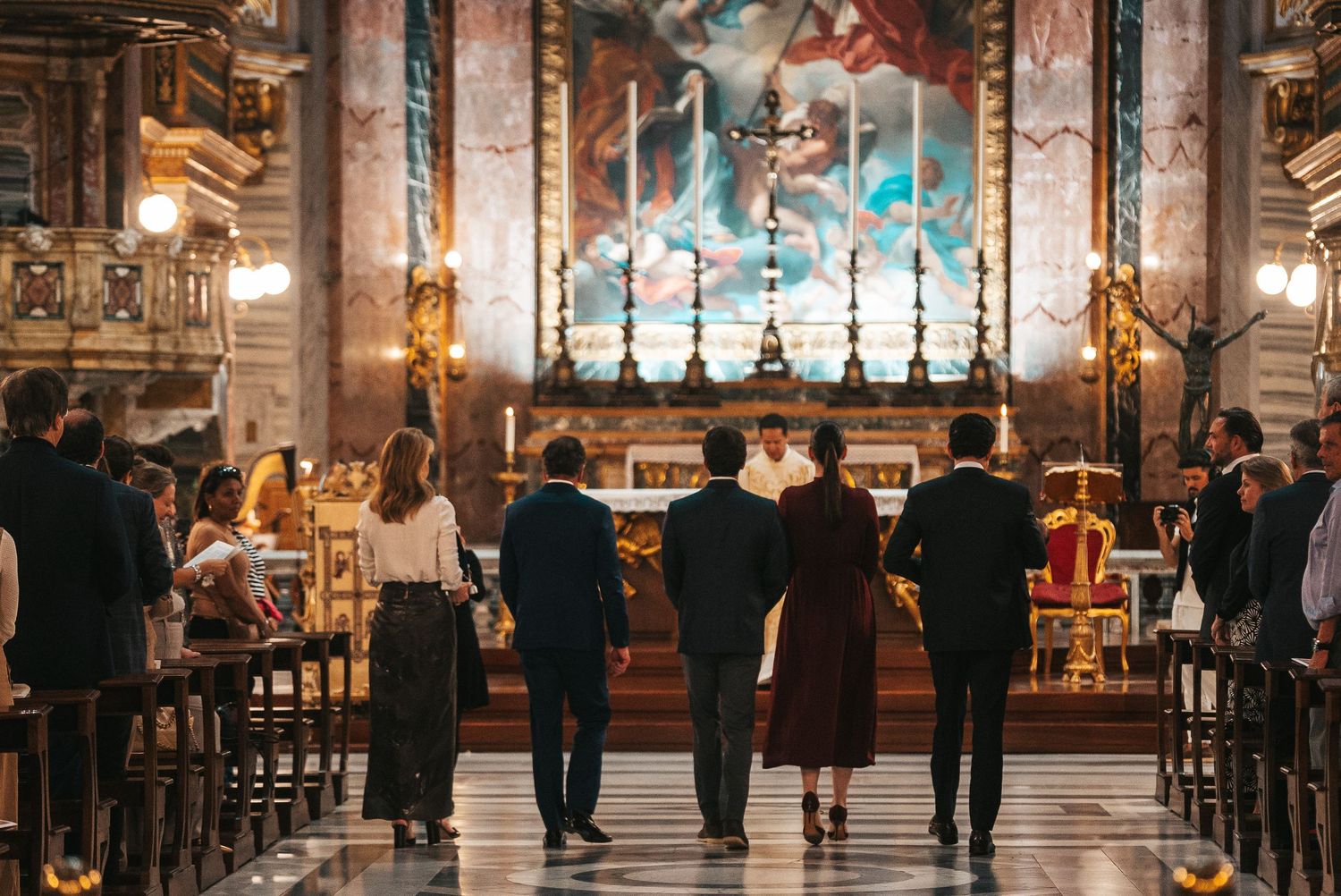 People gather inside an ornate cathedral with high vaulted ceilings, marble columns and religious artwork during a service.