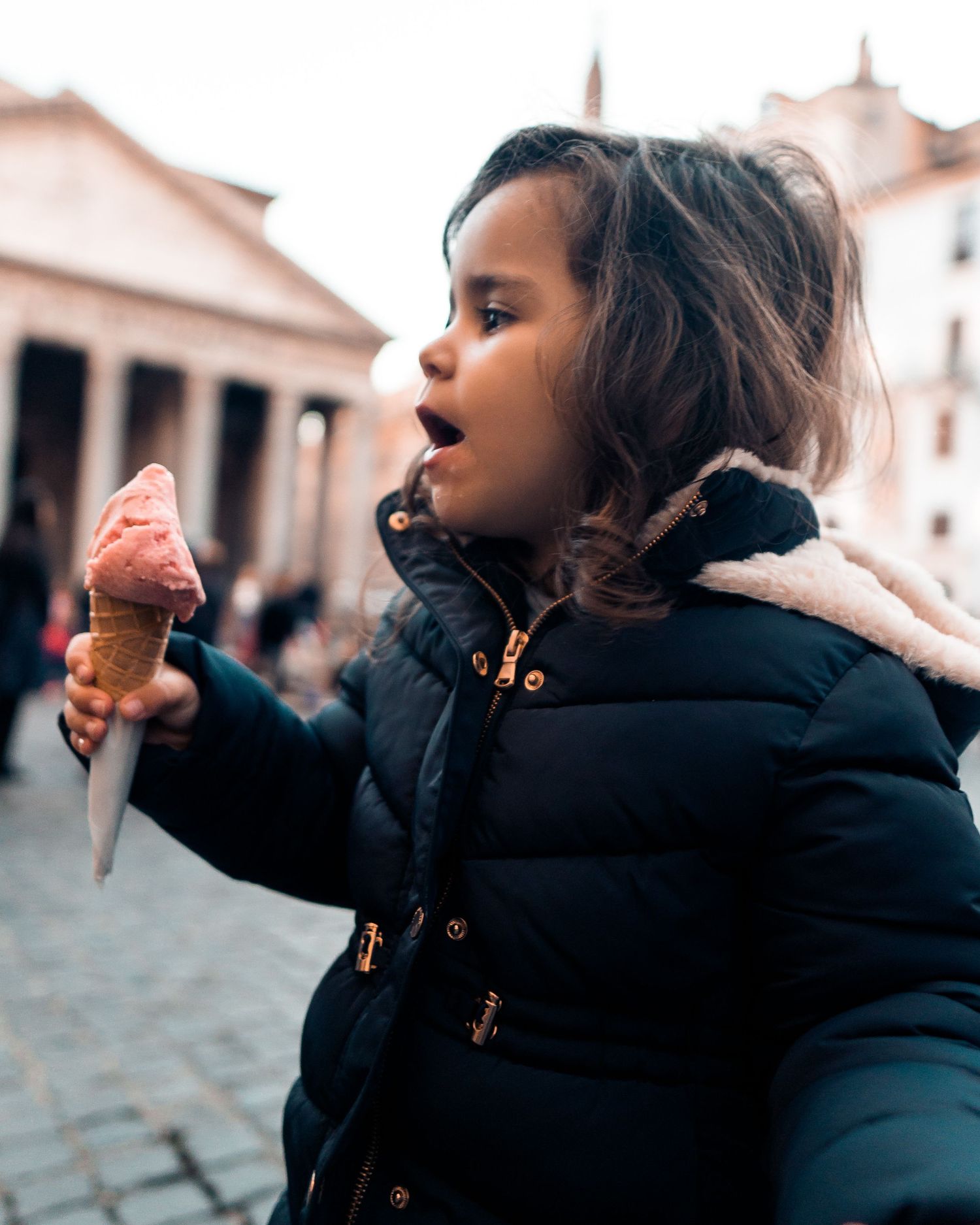 Someone in a winter coat enjoys a gelato ice cream cone while standing in front of the Pantheon in Rome.