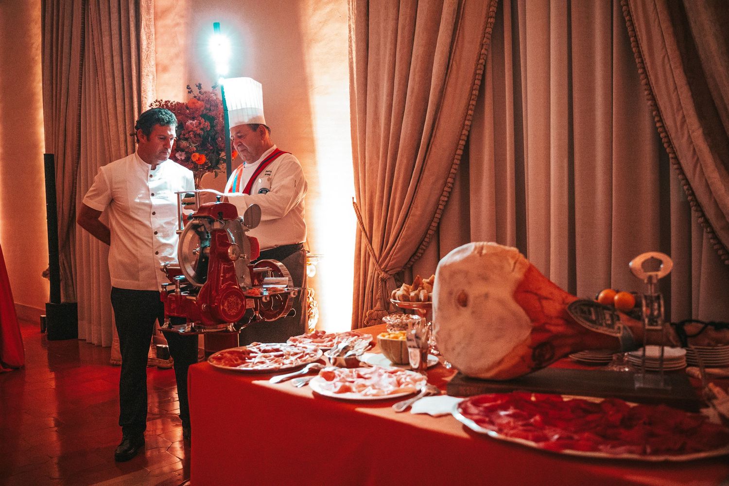 Panoramic view of an elegant dining room with red lighting, white curtains, and formal table settings.