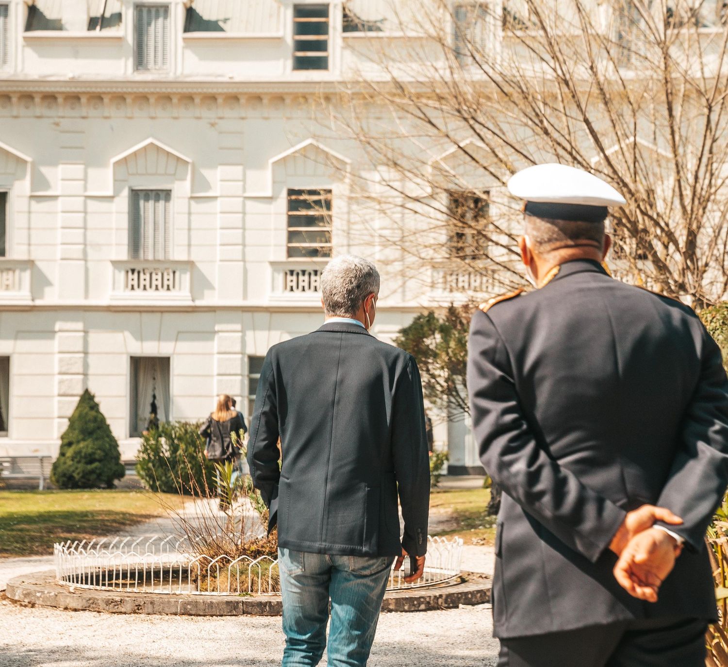 A series of people walking along a sidewalk in front of a white building on a winter day.