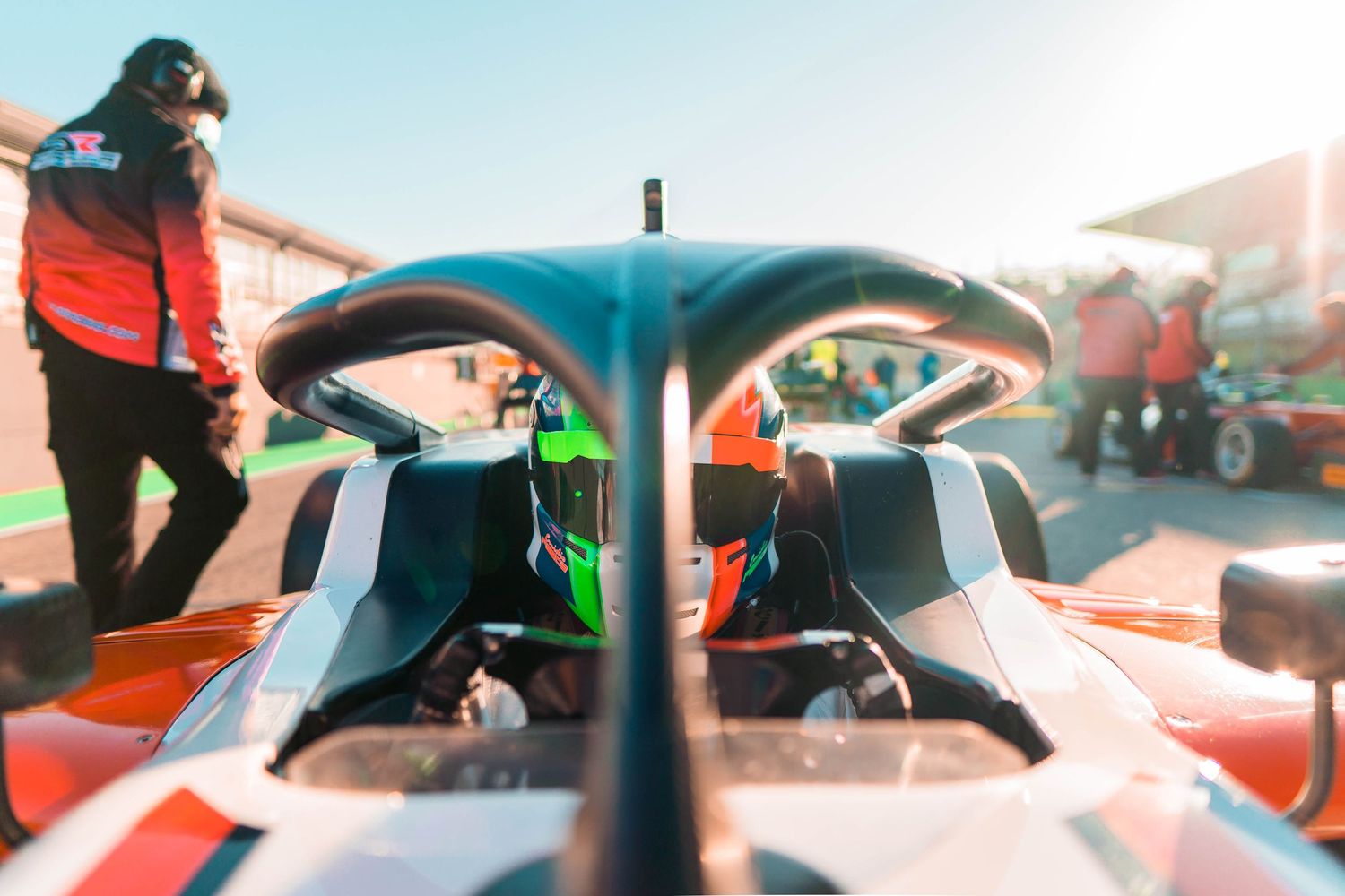 Aerial view of race cars lined up on a sunny track with pit crews and team members preparing for competition.