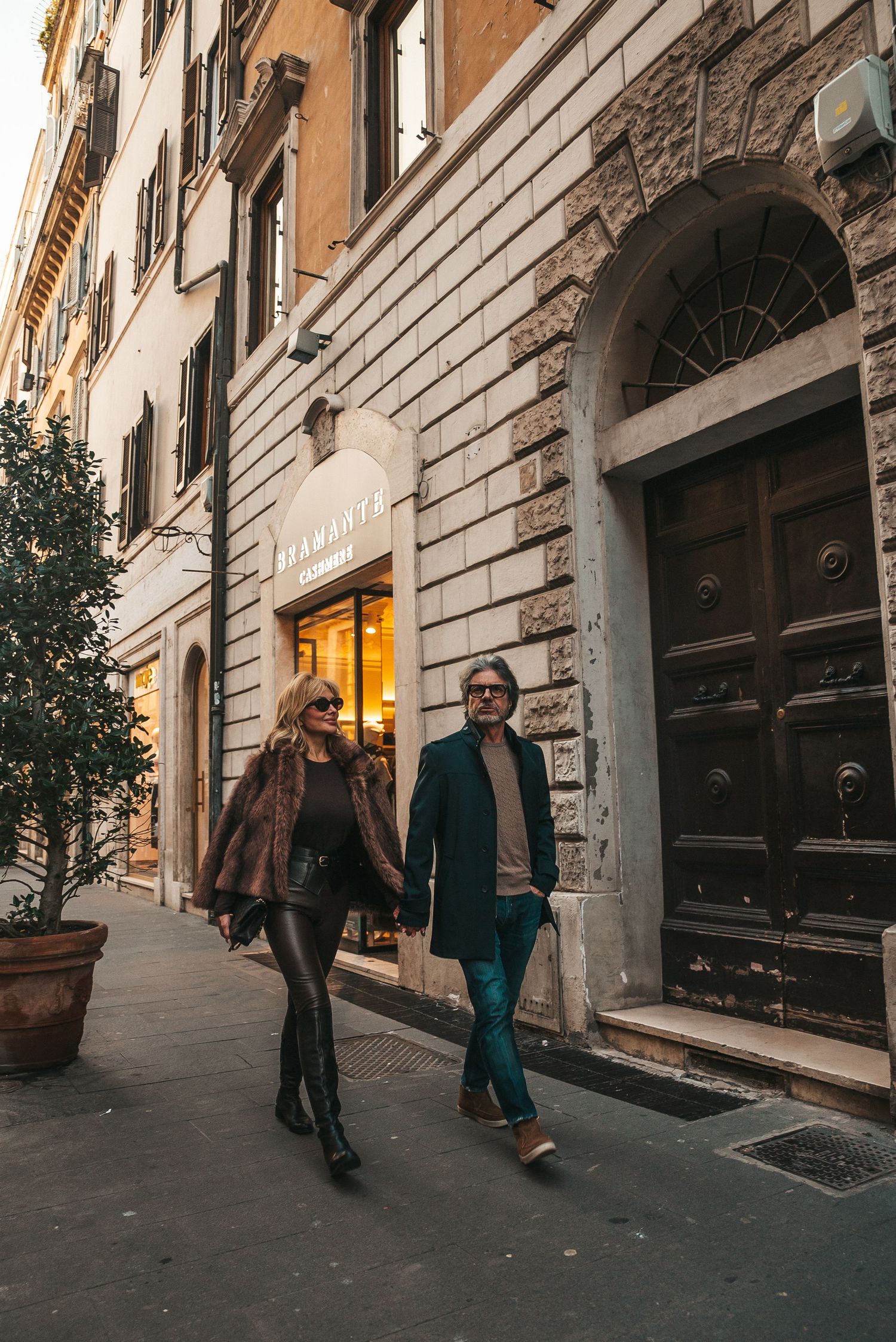 People walking along a historic cobblestone street with classic Italian architecture and arched doorways.