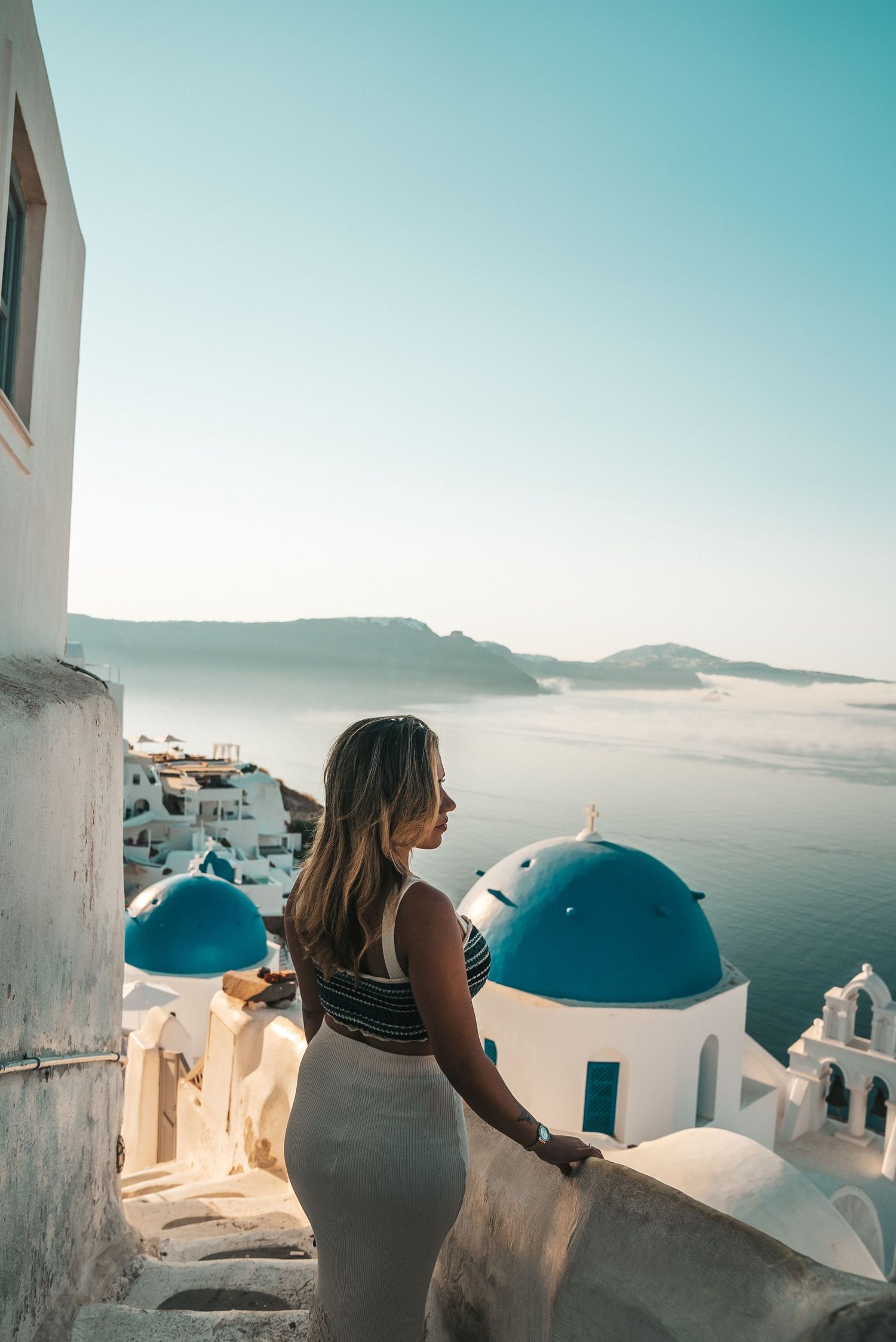 A person admires the stunning blue-domed churches and white architecture of Santorini, Greece at sunset.