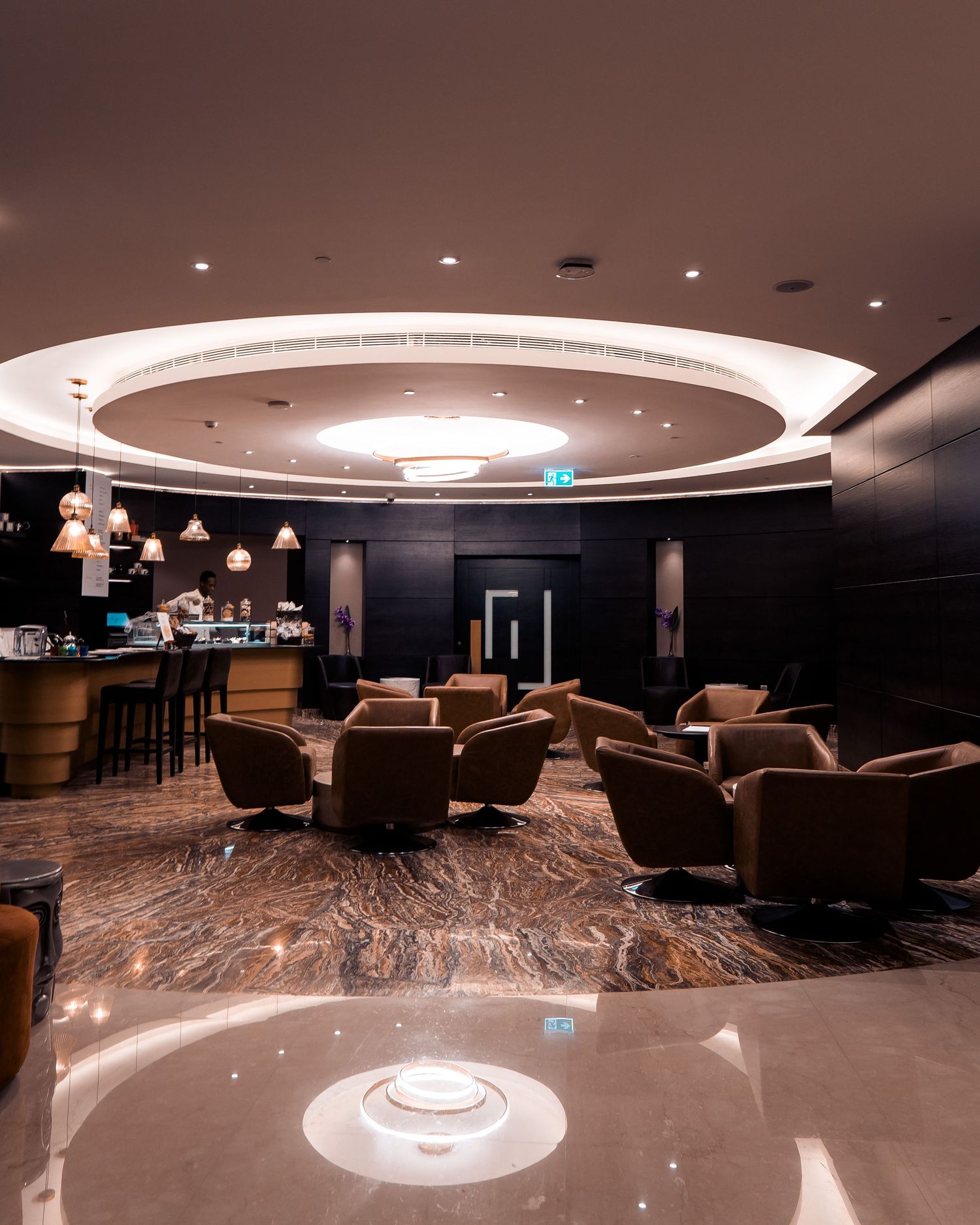 Modern lounge interior with circular ceiling design, leather seating, and marble flooring in elegant brown tones.