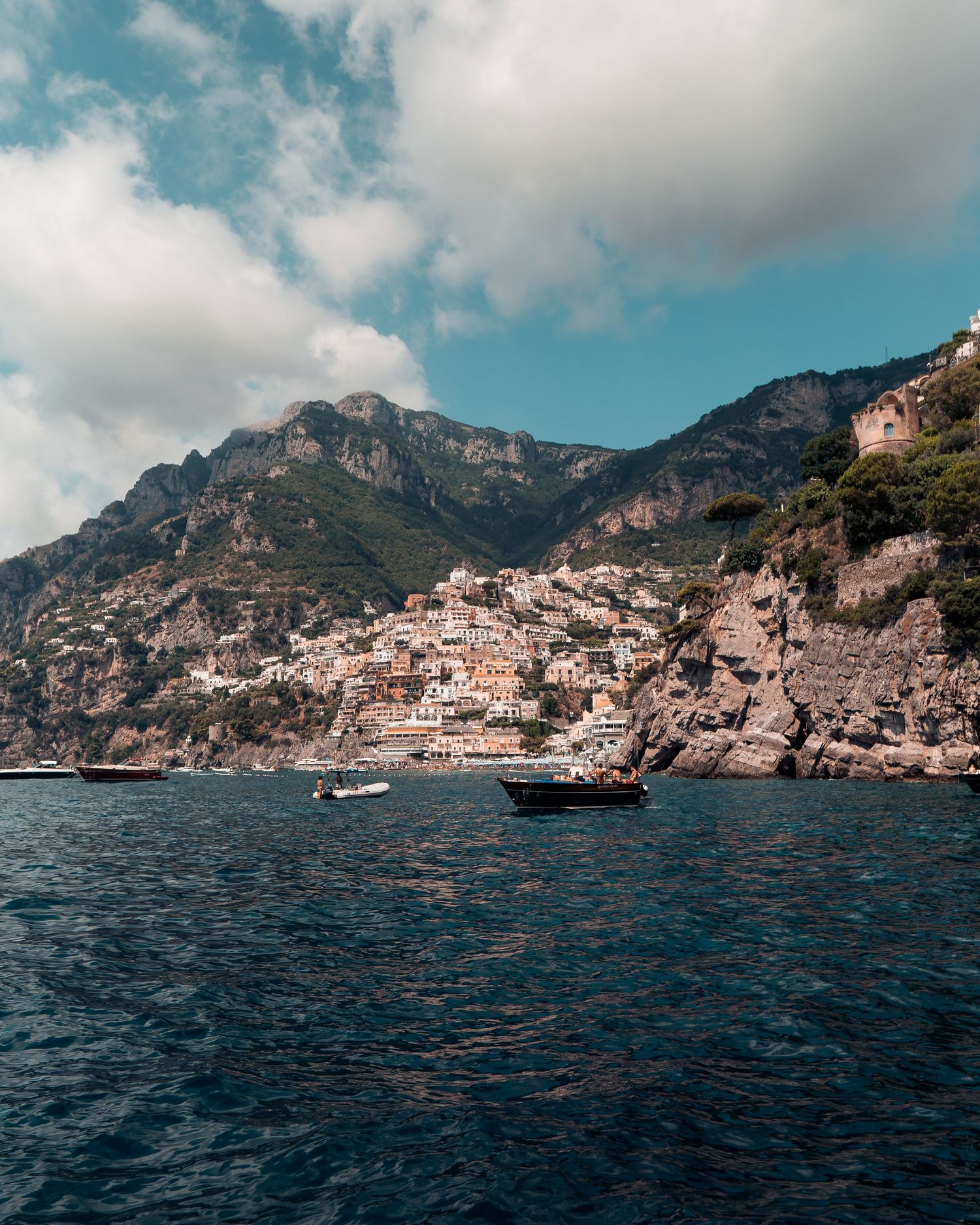 Panoramic view of the rugged Amalfi Coast with dramatic cliffs rising from deep blue Mediterranean waters.