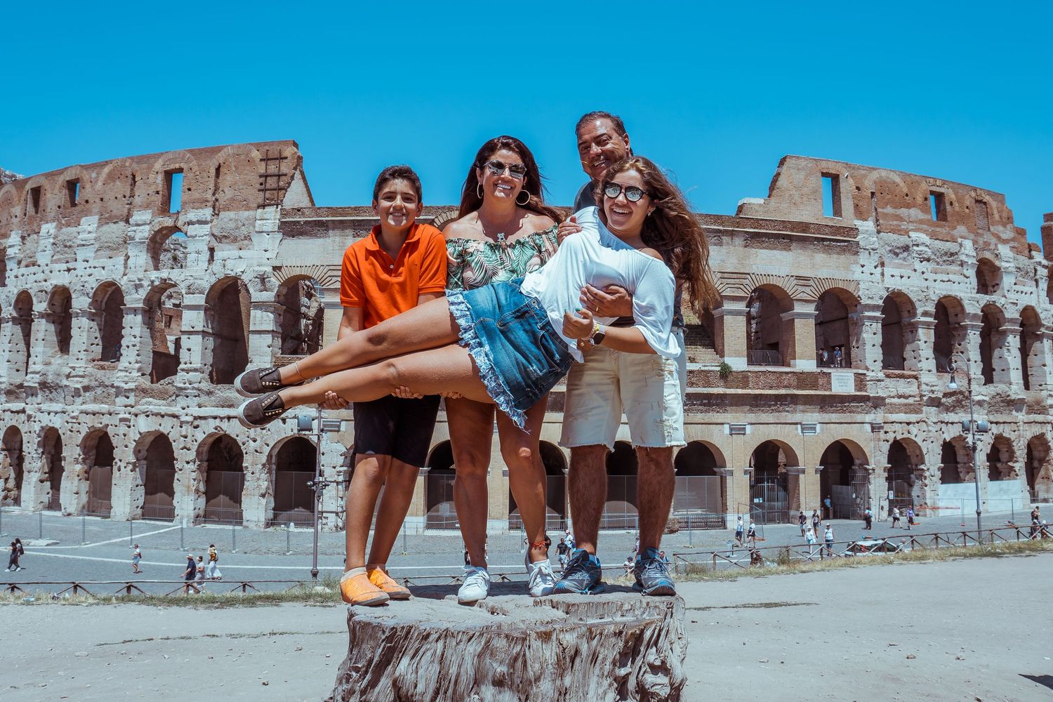 Group of tourists posing playfully in front of the ancient Roman Colosseum on a sunny day in Italy.