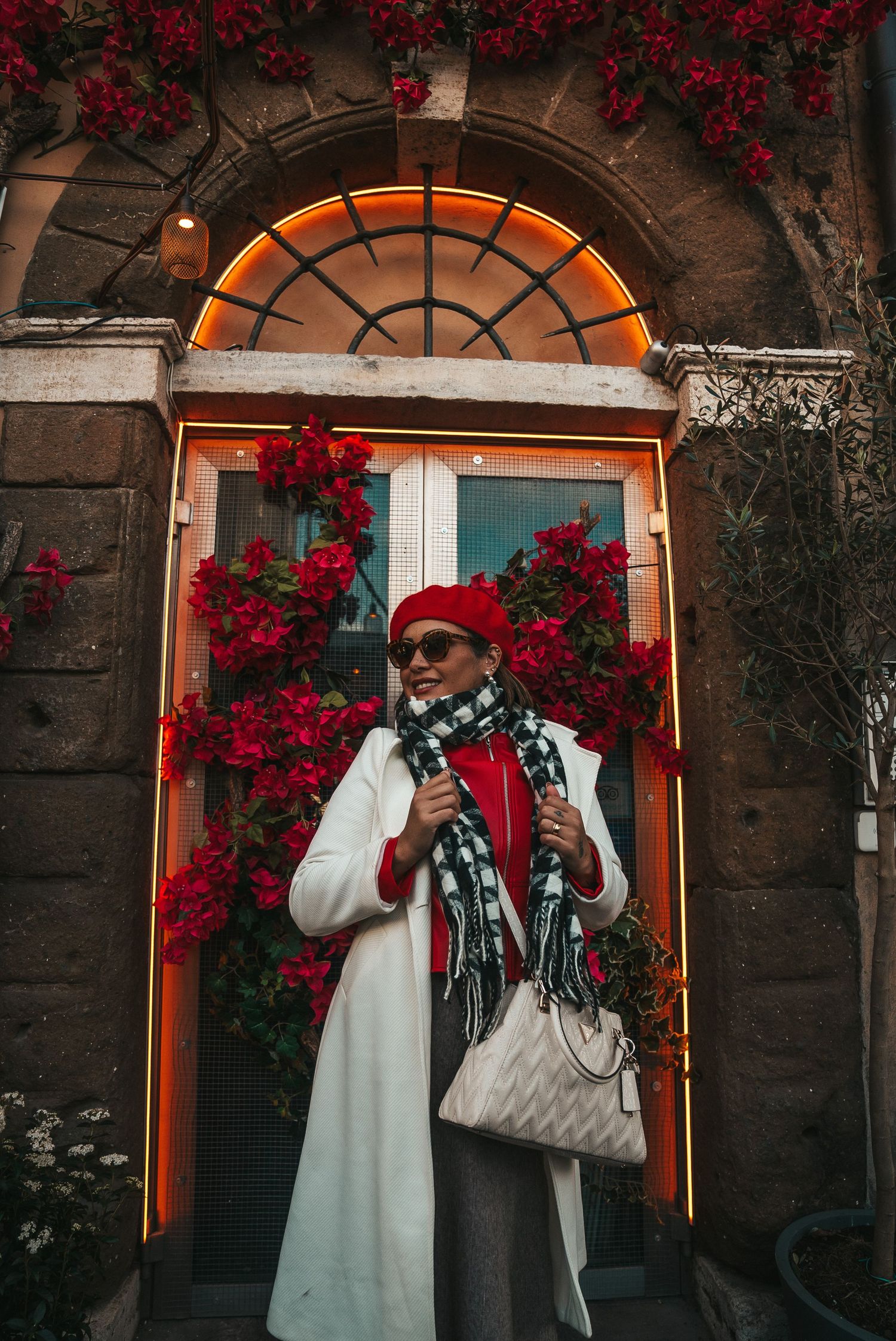Stylish winter outfit captured in front of a doorway adorned with vibrant red bougainvillea flowers.