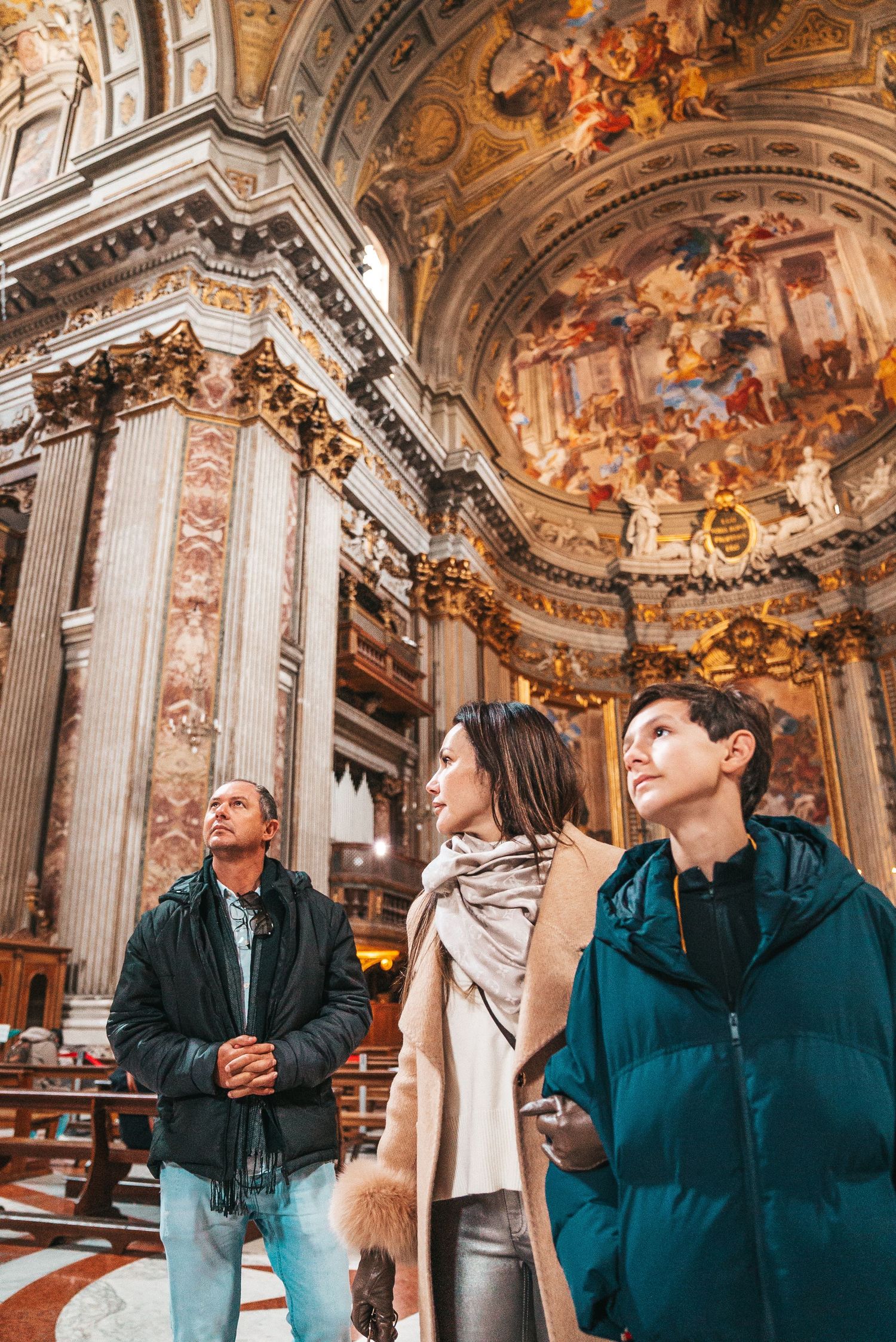 Tourists admiring ornate ceiling frescoes inside historic Roman church.