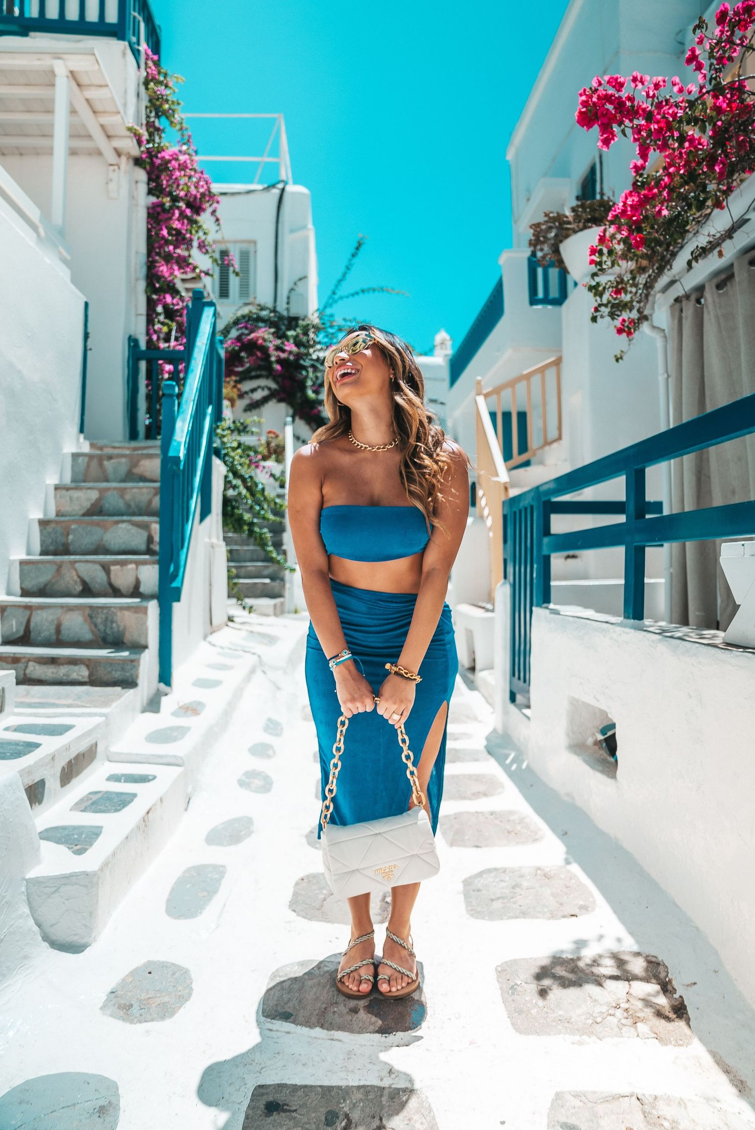 A scenic view of traditional white Cycladic architecture in Mykonos with pink bougainvillea flowers and cobblestone steps.