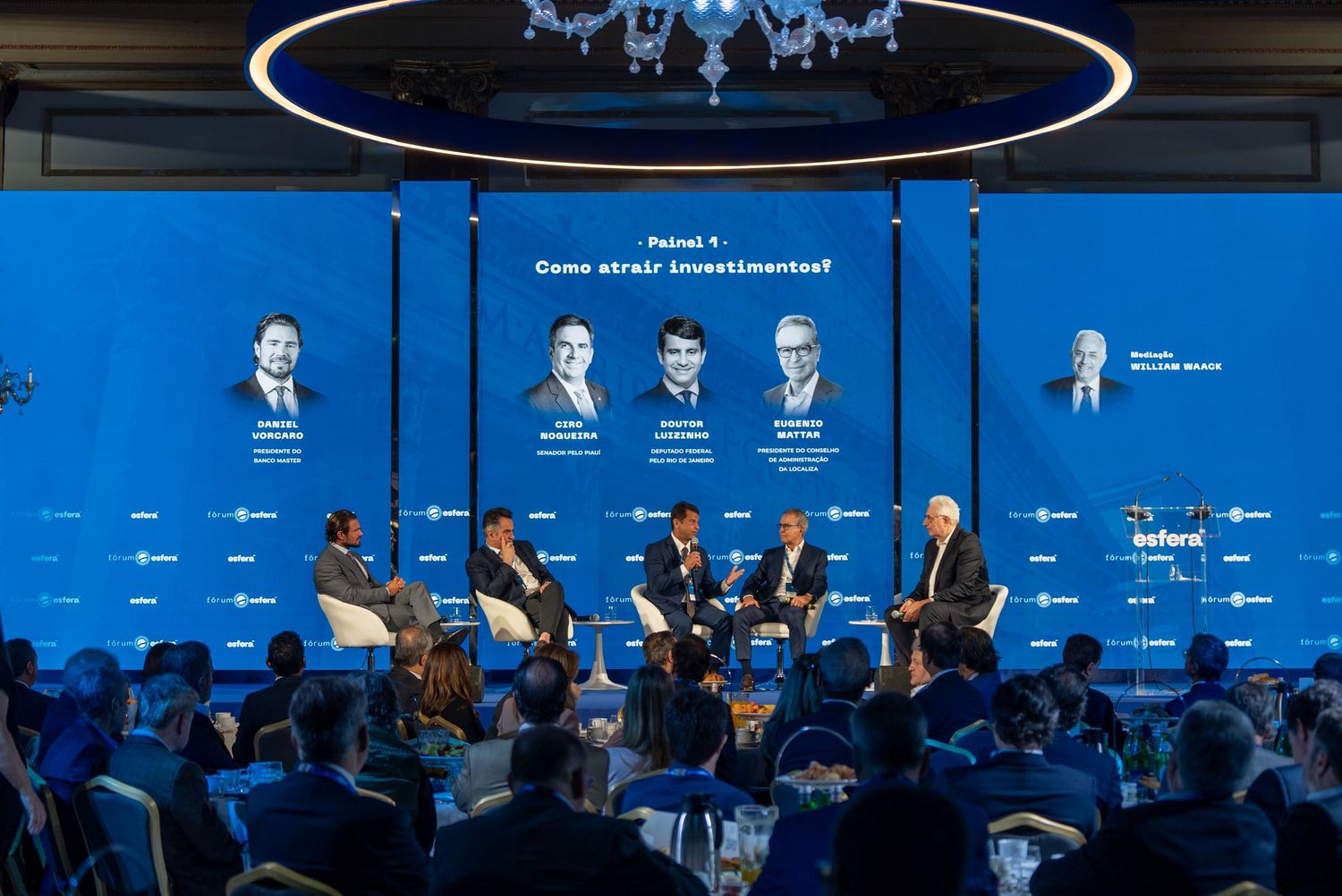 Professional conference panel discussion with speakers seated on stage against a blue backdrop at an industry event.
