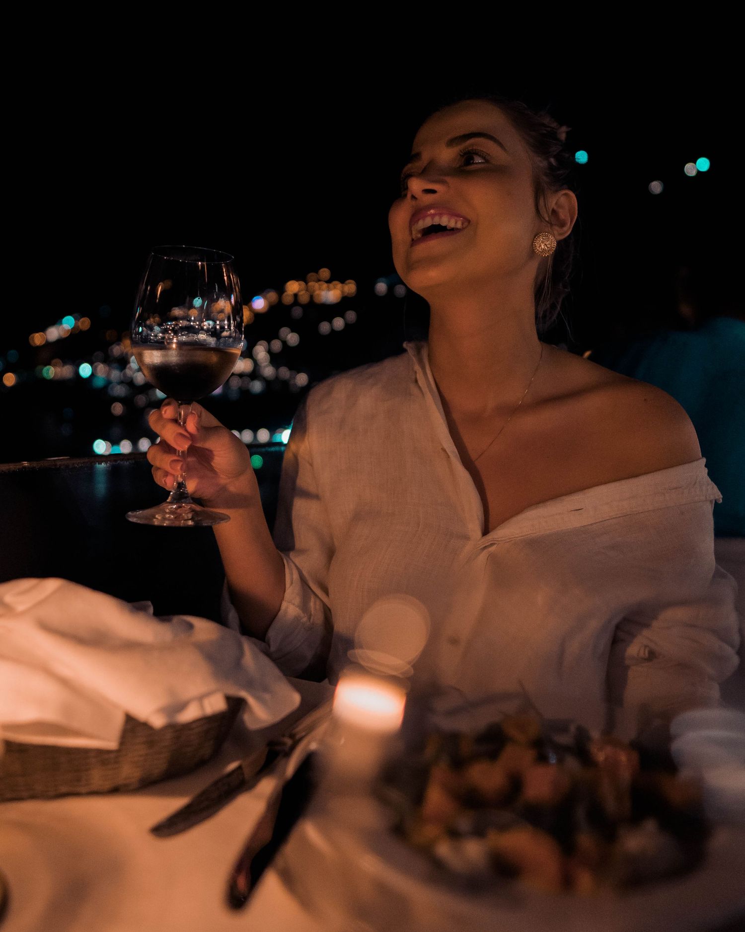 Person enjoying a candlelit dinner at night with blurred city lights visible in the background.