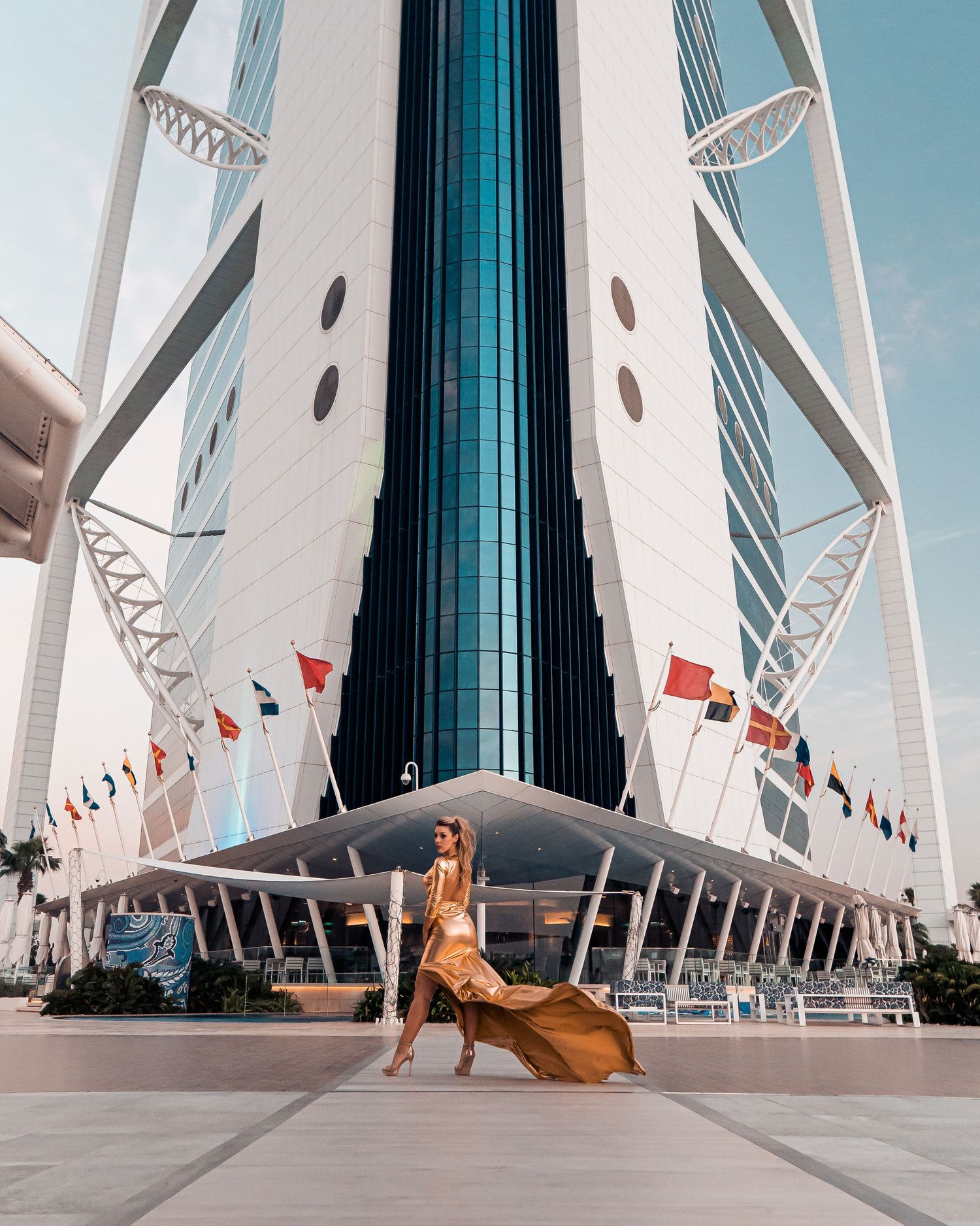 A person in a flowing dress poses dramatically in front of the Burj Al Arab luxury hotel in Dubai.
