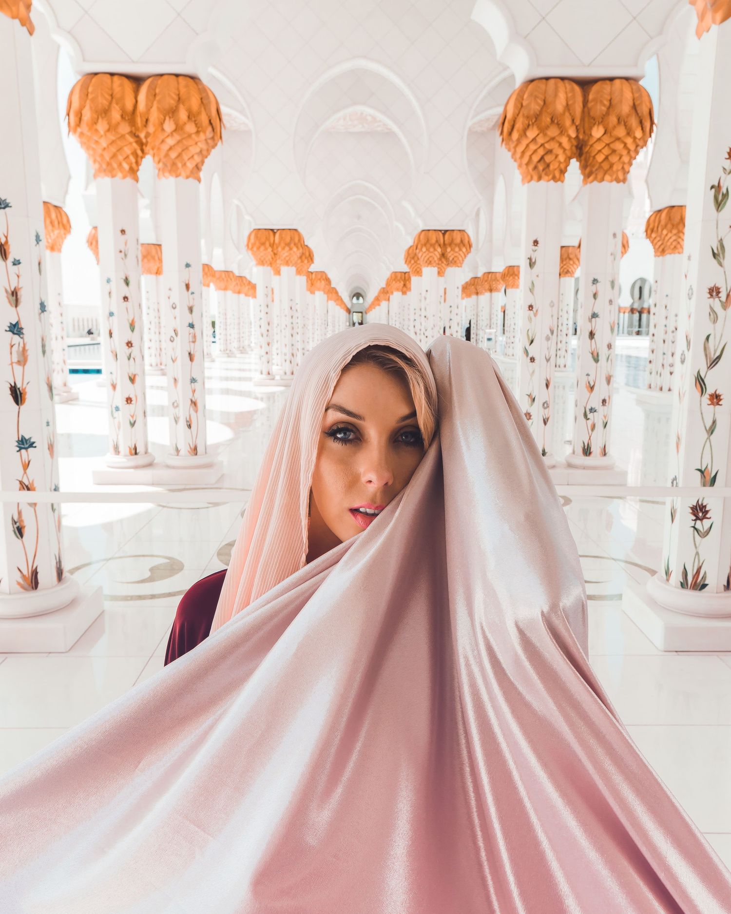 Artistic portrait in Sheikh Zayed Mosque featuring flowing white fabric and orange decorative lights.