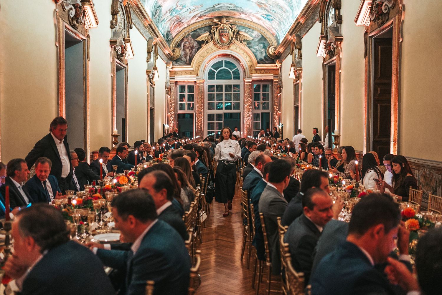 Elegant formal dinner event in a grand historic hall with ornate architecture and long tables filled with guests.