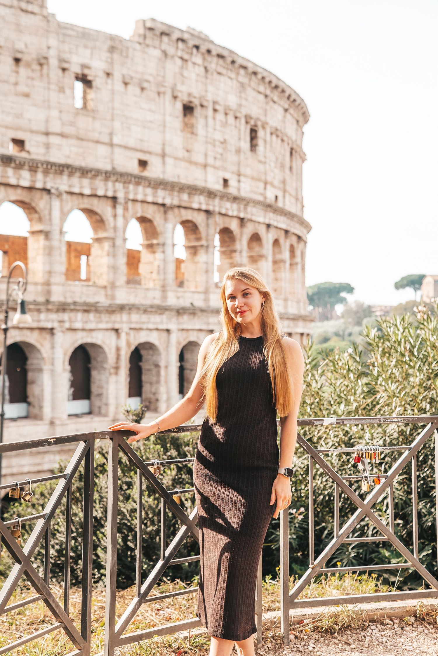 Woman in black dress poses near the iconic Roman Colosseum at sunset.