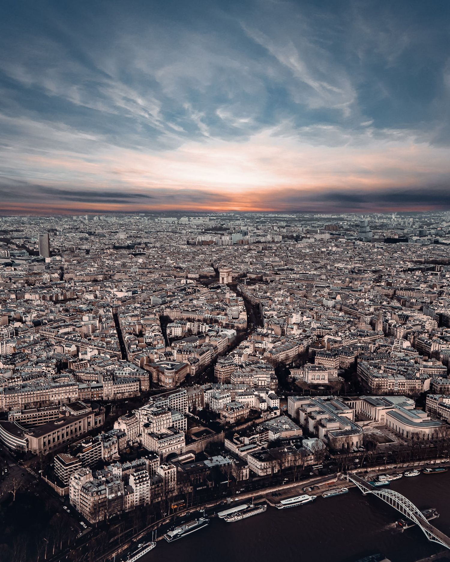 Panoramic aerial view of Paris cityscape at sunset with dramatic cloudy sky and historic architecture stretching to horizon.