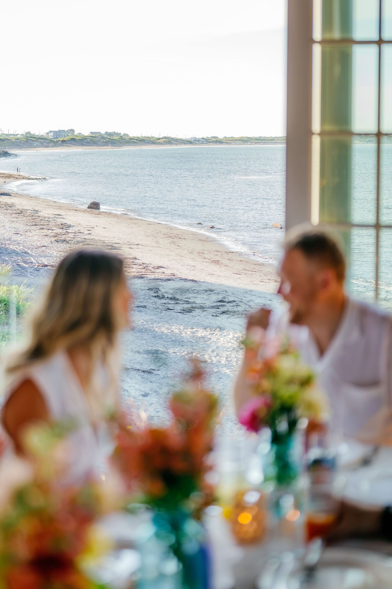 Couple dining at a beachside restaurant with colorful flowers and ocean views in the background.