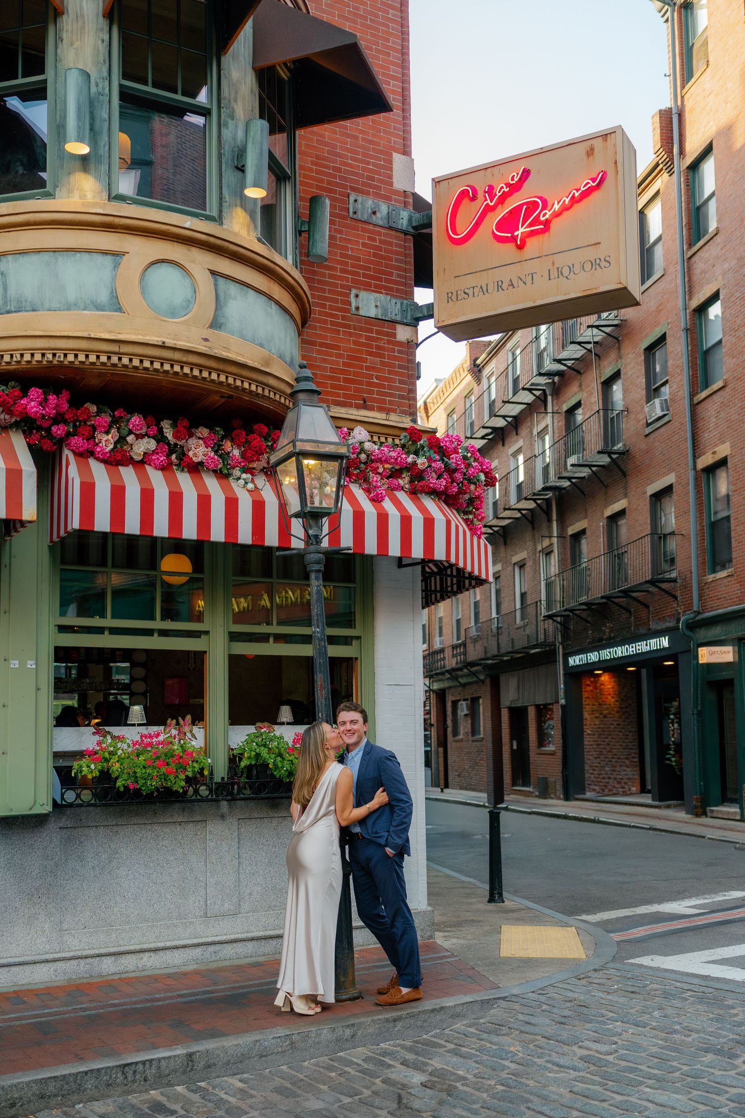 Couple embracing under a gas lamp on a cobblestone street outside Cia Rou restaurant with red striped awnings.
