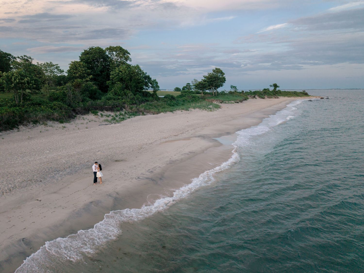 Drone view of a couple walking along the beach during a Harkness Memorial State Park engagement session on the Connecticut shoreline.