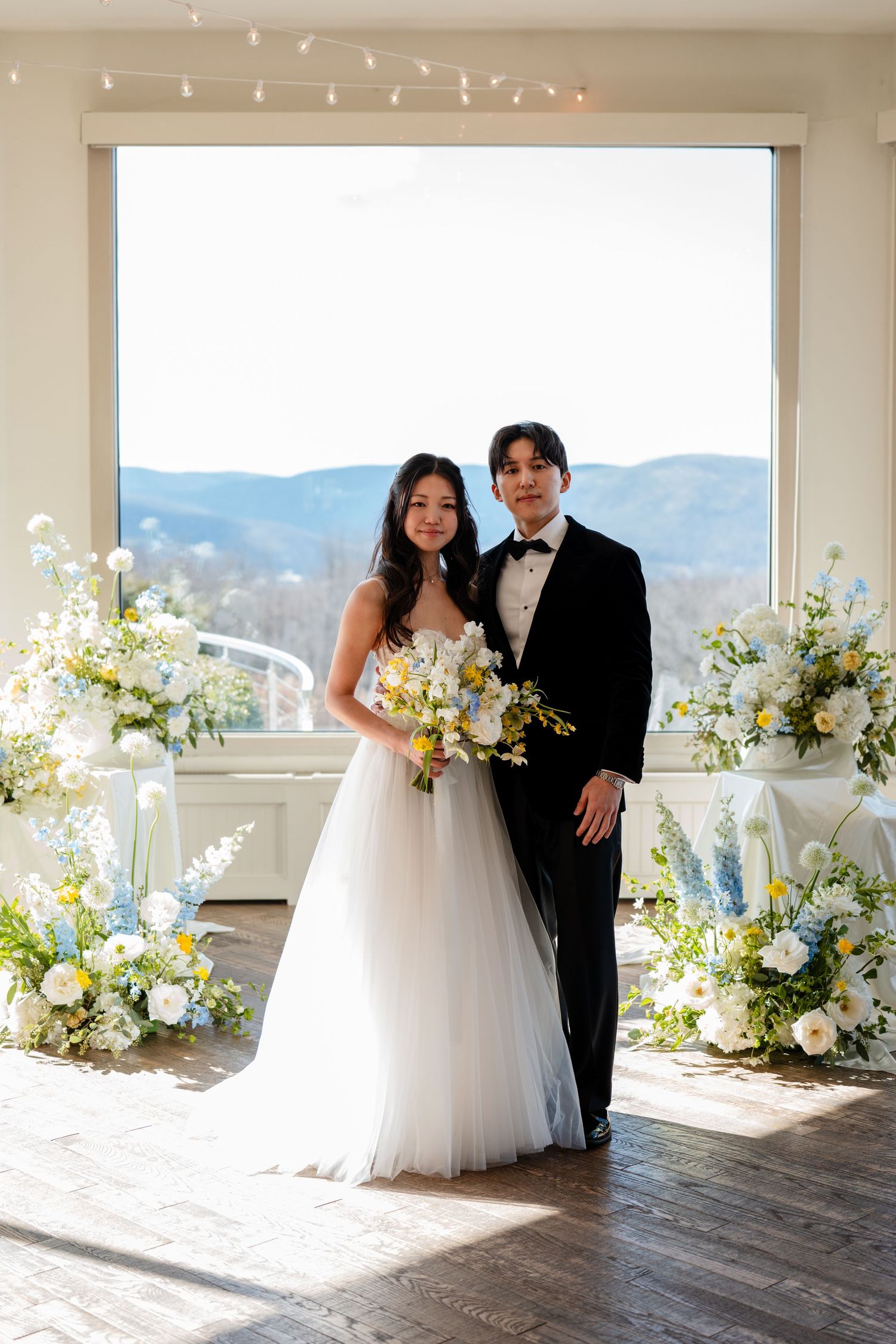 Bride and groom posing together after their wedding ceremony with floral arrangements and mountain views.