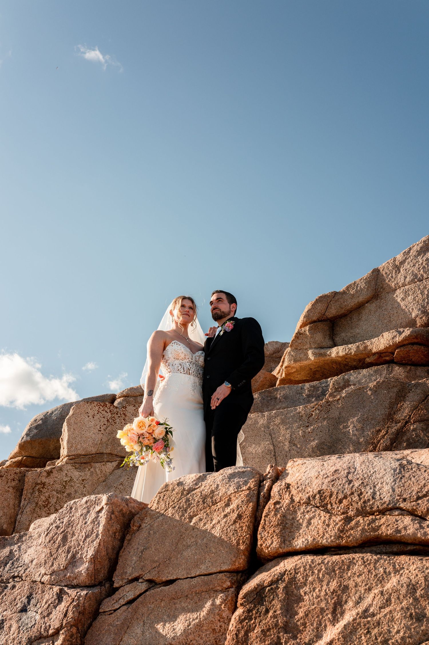 Bride and groom standing on coastal cliffs during a destination wedding portrait session.