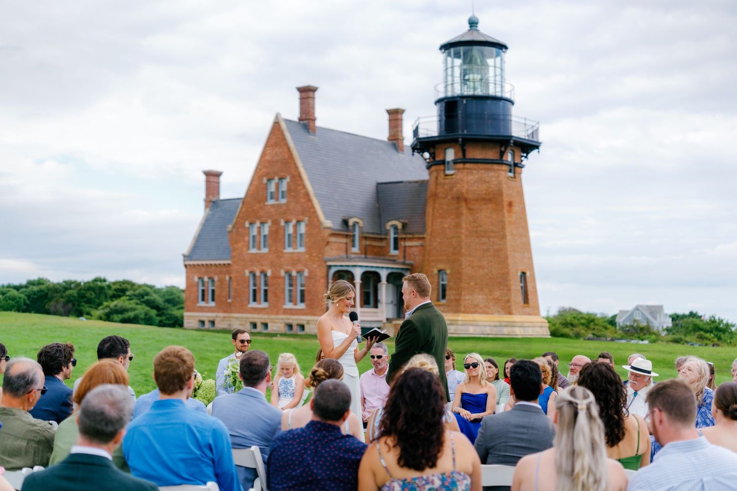 Outdoor wedding ceremony on green lawn before historic brick Block Island Southeast Lighthouse, Rhode Island.