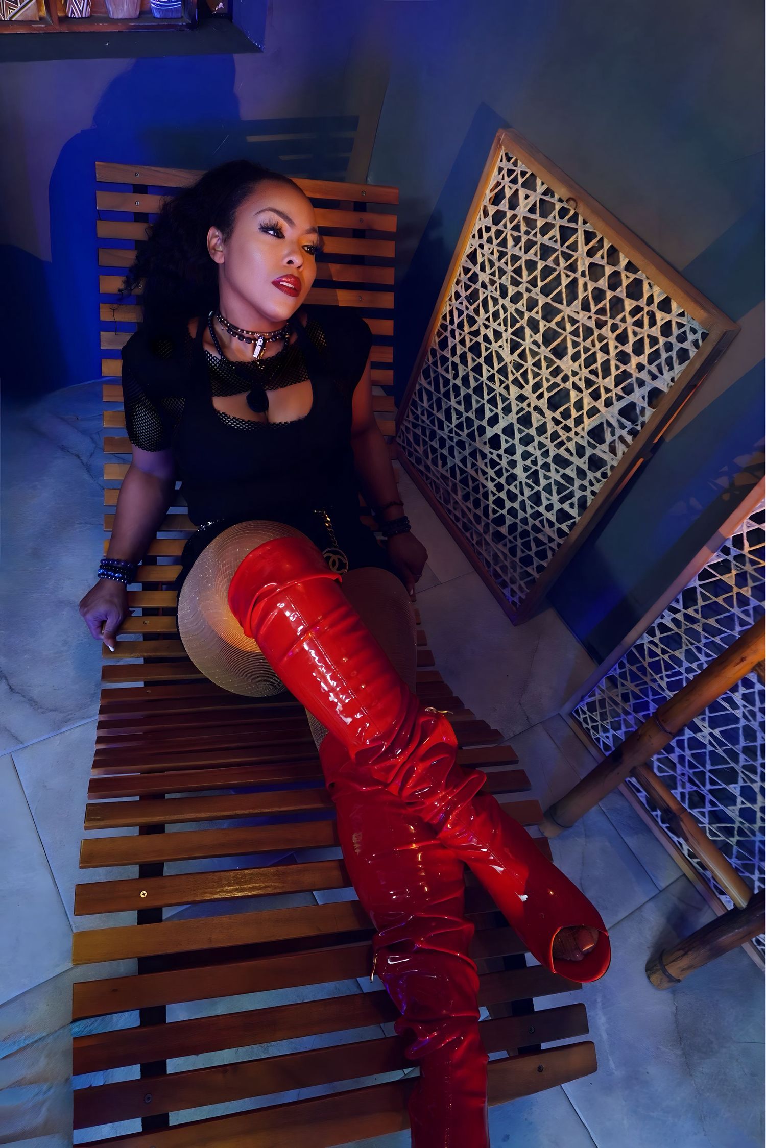 A figure in black and red latex poses dramatically on wooden steps with geometric lighting in the background.
