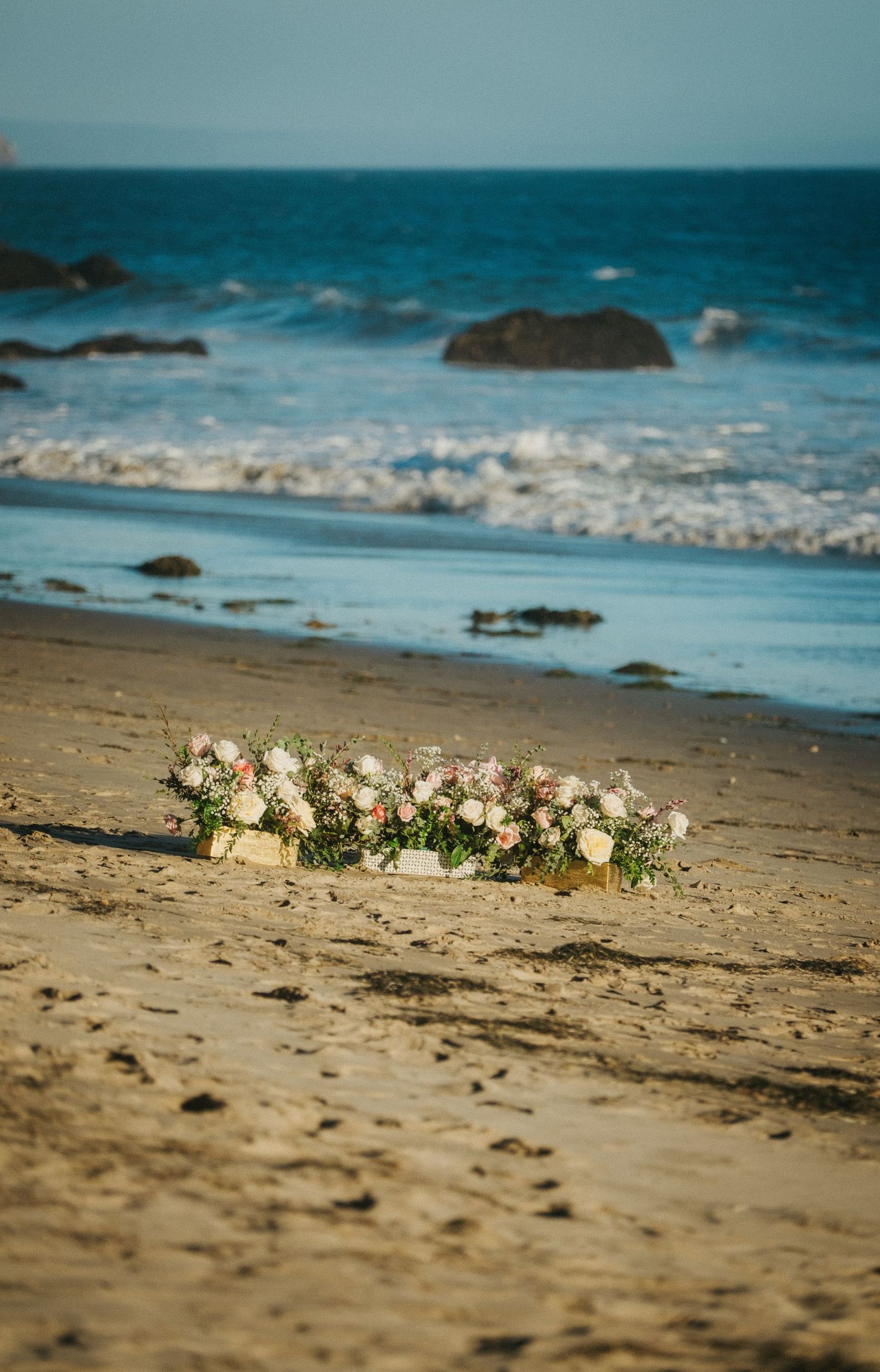 Floral arrangement of pink and white roses placed on sandy beach.