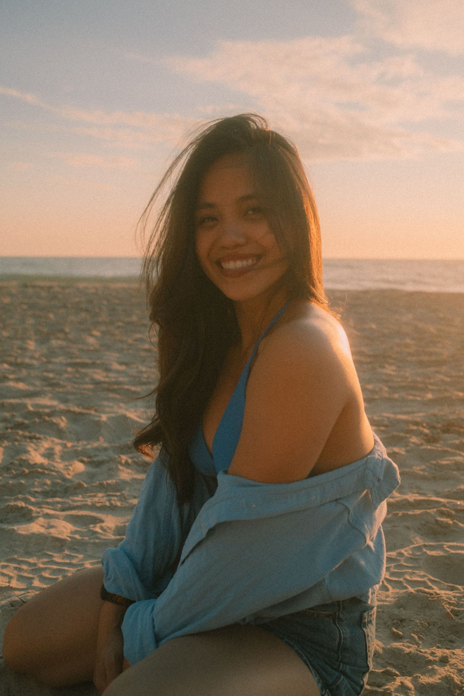 Smiling young woman in blue bikini top and shirt on beach at golden hour.