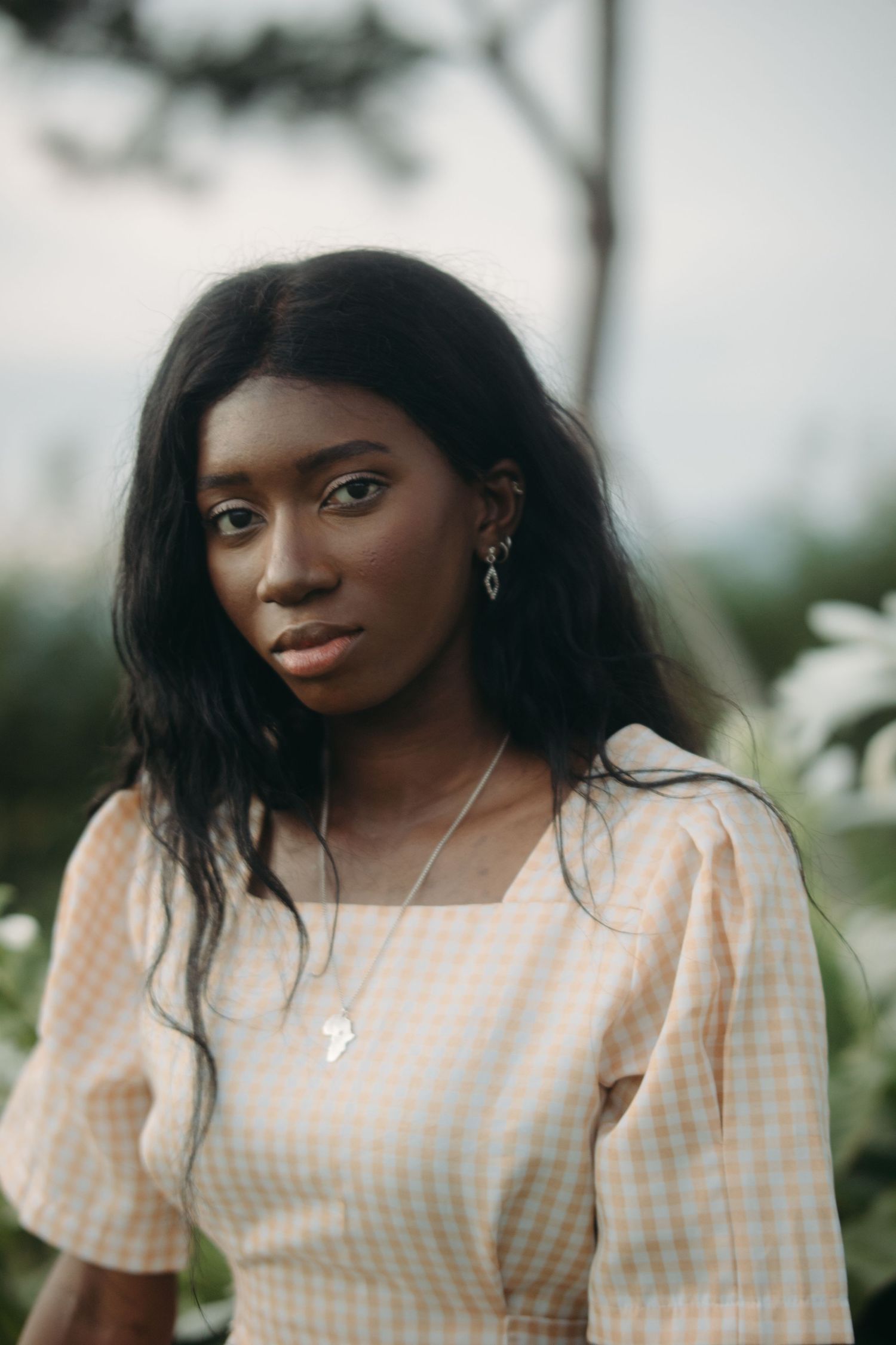Close-up portrait of young Black woman in plaid dress with necklace outdoors.