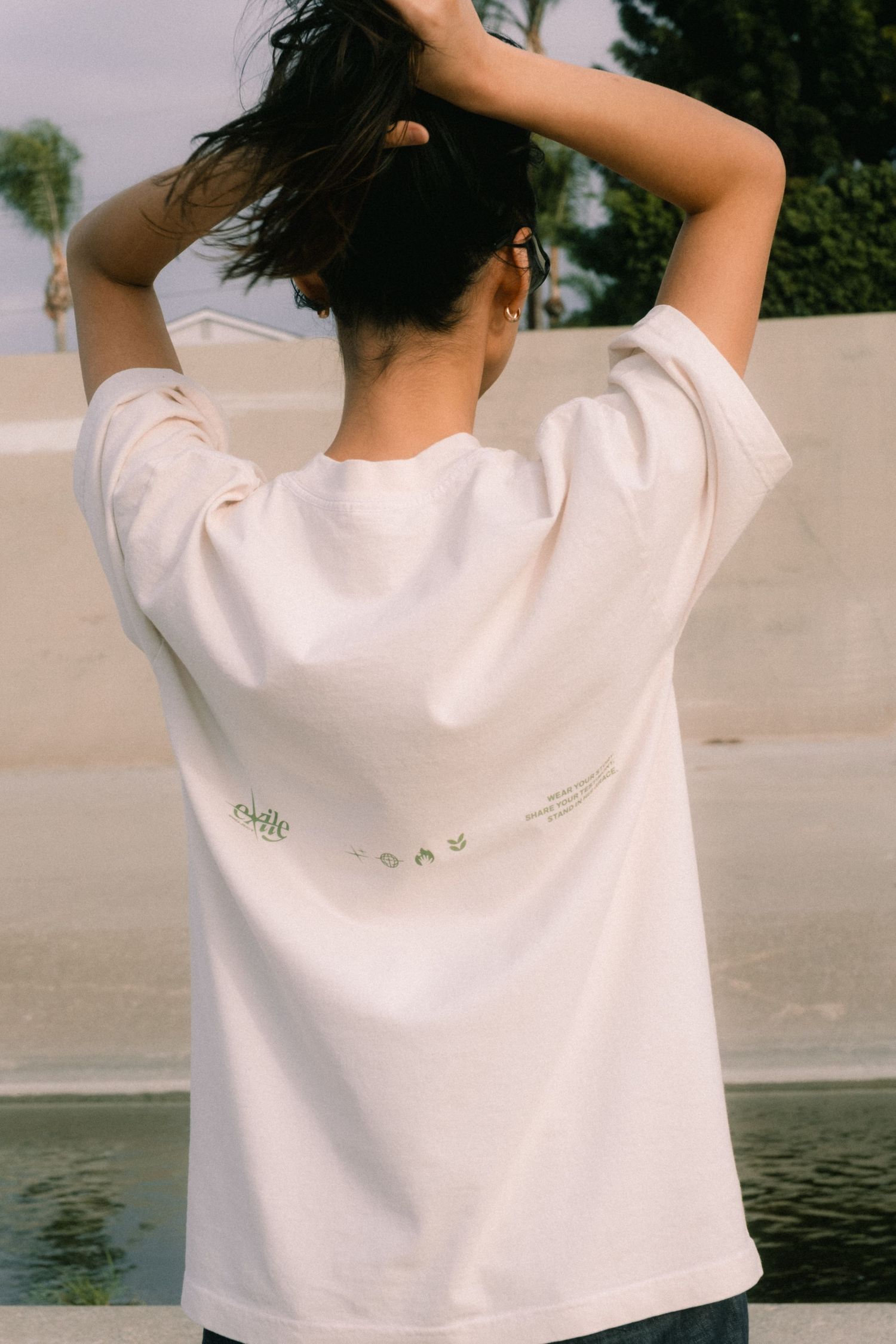 Back view of a woman wearing an oversized cream graphic t-shirt outdoors near a pool.