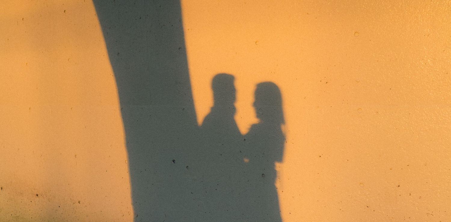 Shadow silhouette of a romantic couple standing together on a warm golden yellow wall.