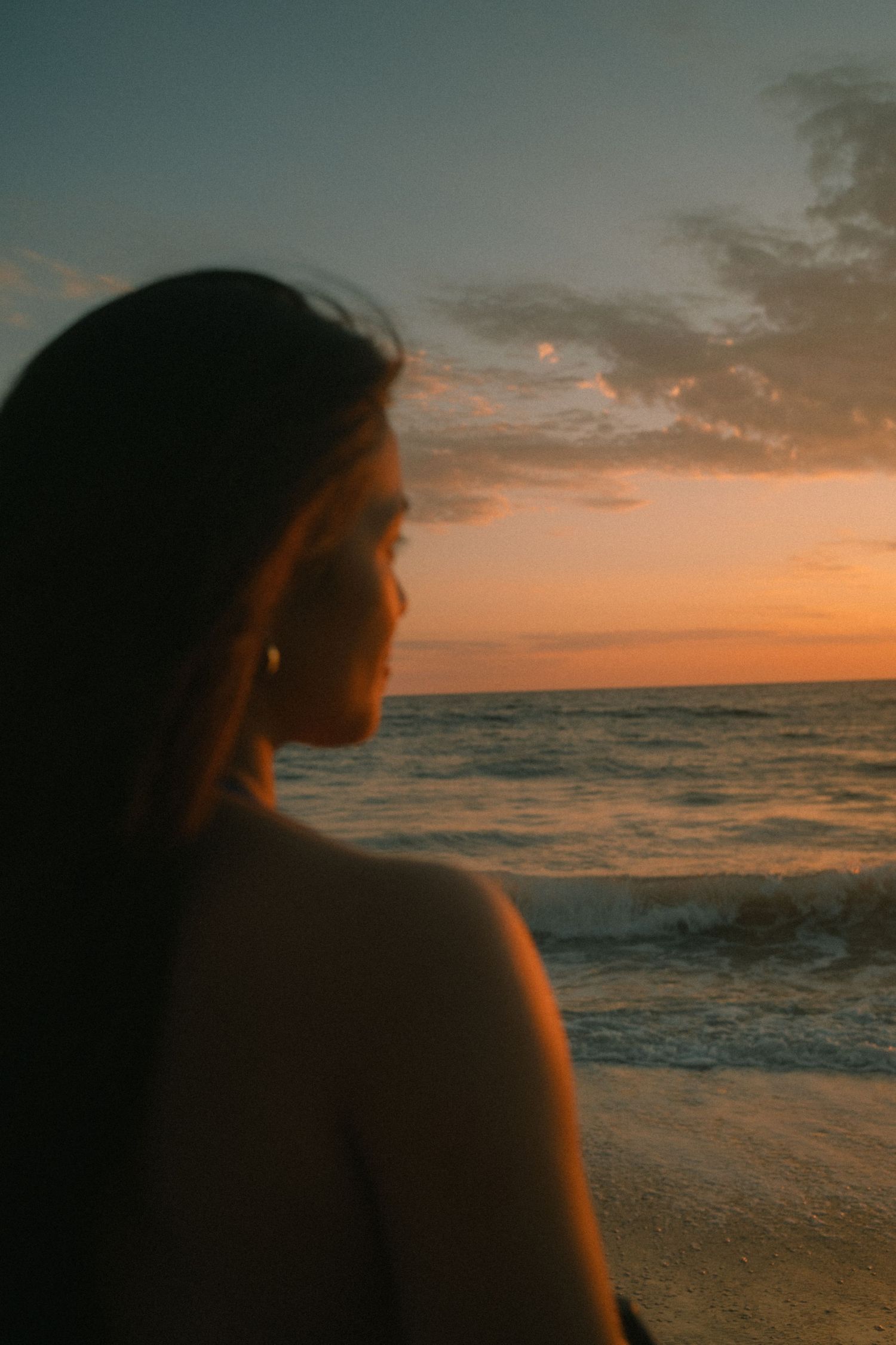 Woman gazing at ocean waves during golden sunset at beach.