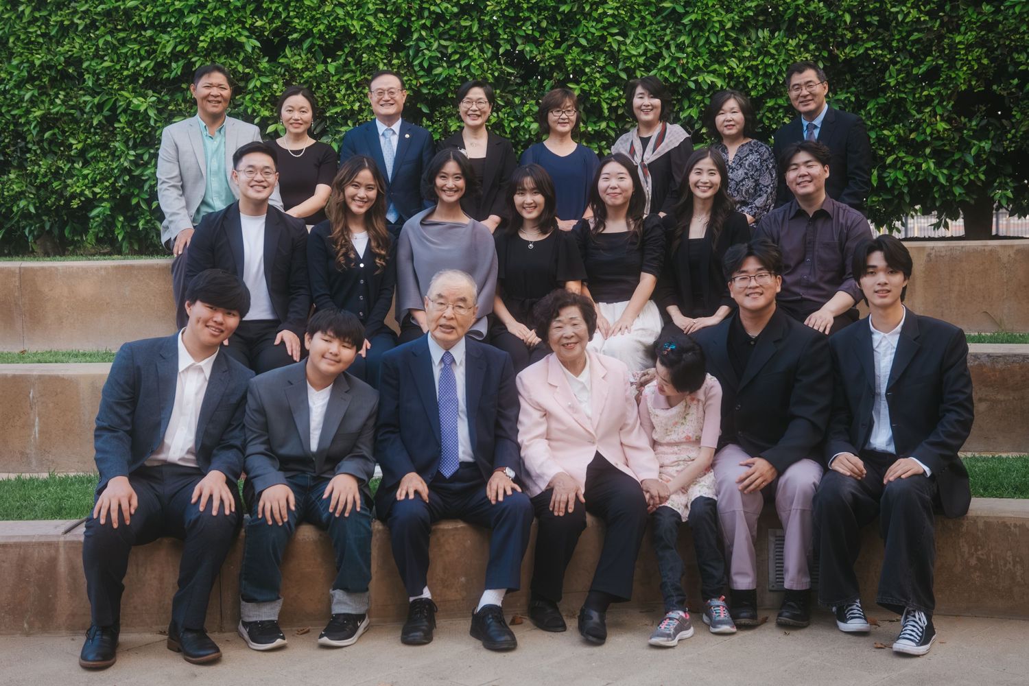 Large group of Asian students and faculty posing together outdoors in front of green ivy wall for formal photo.
