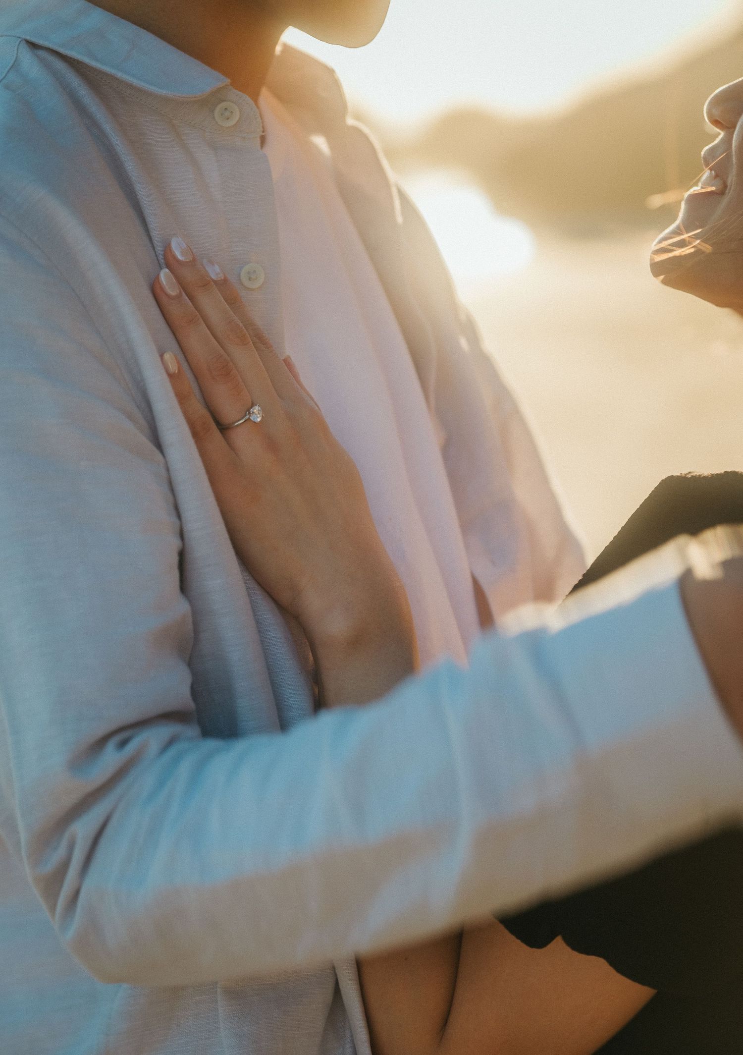 Close-up of a woman's hand with a solitaire engagement ring resting on her partner's chest.
