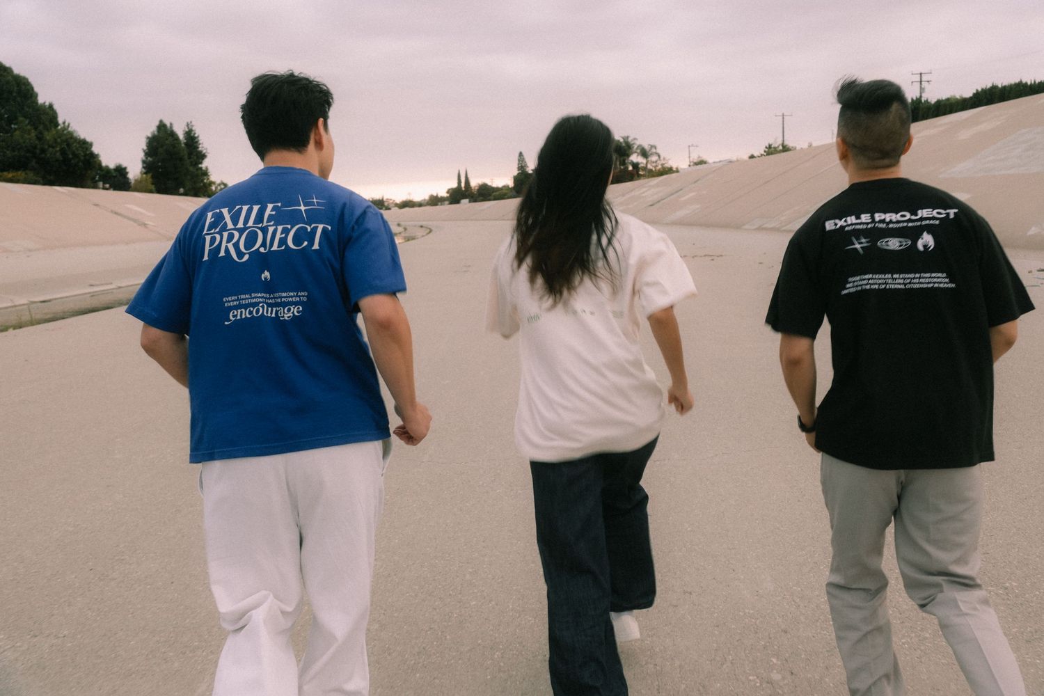 Three friends walking together wearing Exile Project t-shirts in blue, white, and black.