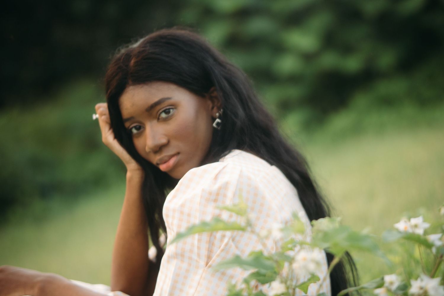 Close portrait of young woman in plaid dress resting head near white flowers.