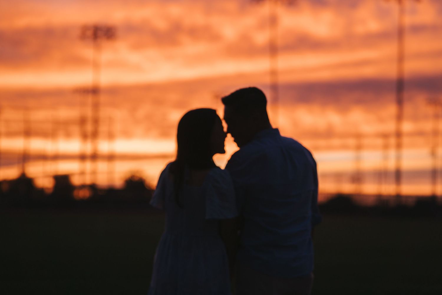 Silhouette of a romantic couple facing each other against a vibrant orange and red sunset sky.