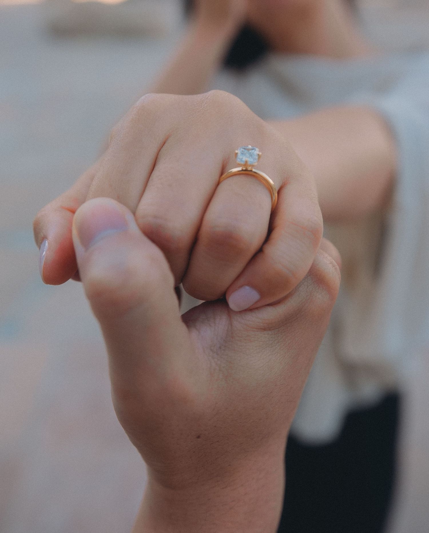 Close-up of a woman's hand wearing a gold diamond engagement ring while holding hands with her partner.
