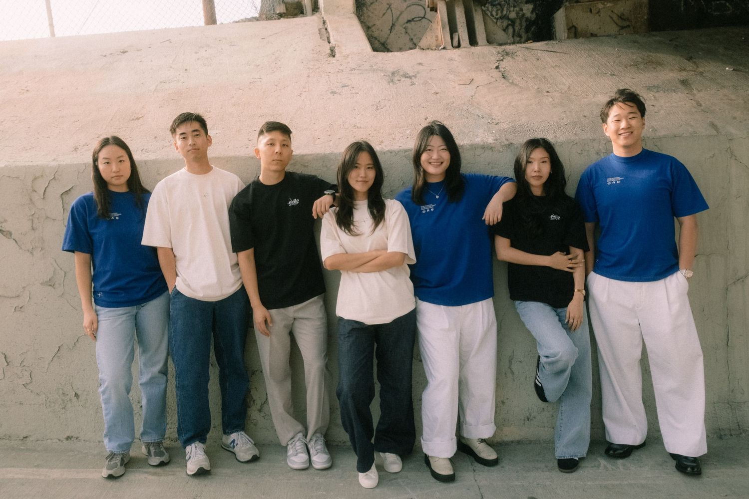 Group of seven young adults in blue and white outfits posing together outdoors.